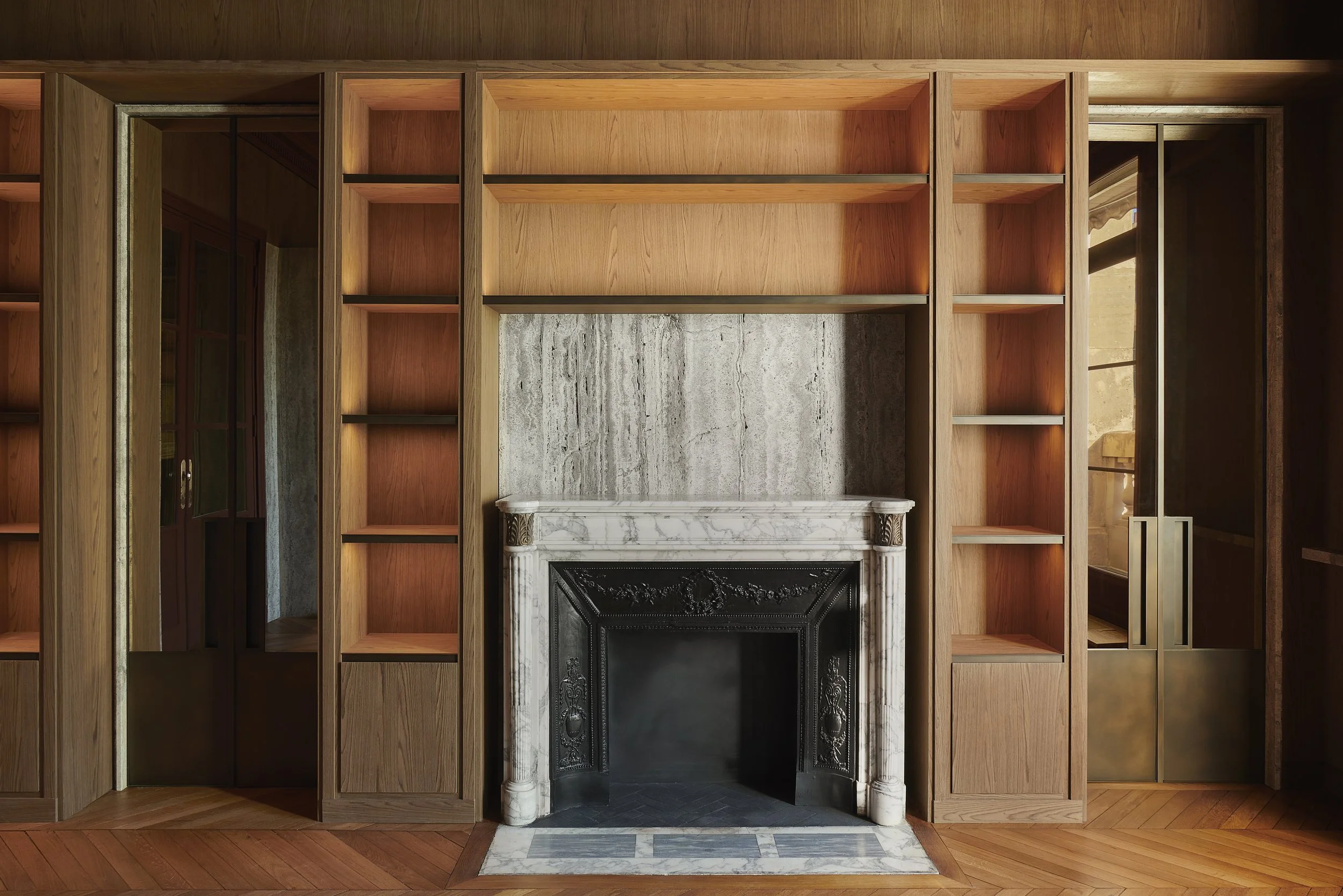 Agencement d'une bibliothèque en chêne avec éclairage, cheminée en marbre d'époque, portes en laiton patiné. réalisation par l'ébéniste agenceur Lamellux