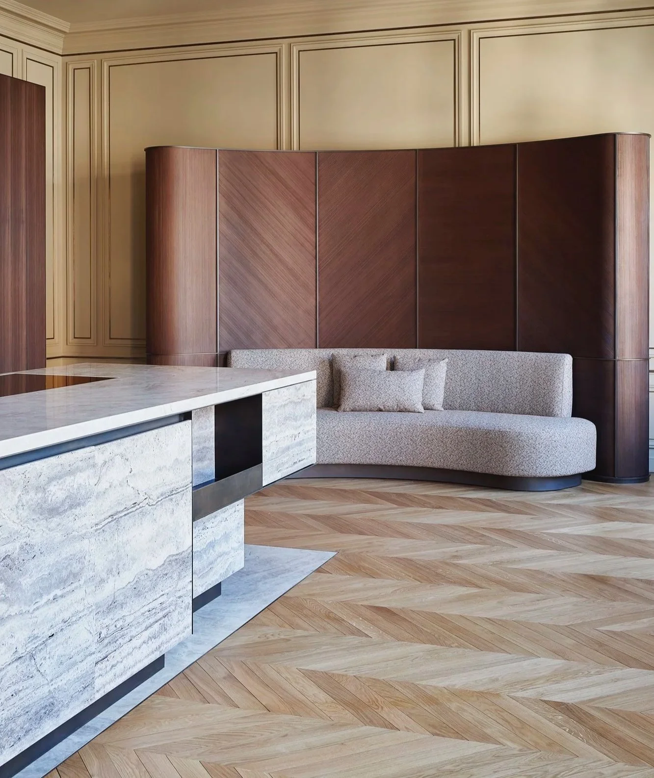 Agencement d'un appartement parisien avec une cuisine en travertin et laiton patiné, sofa sur mesure et boiserie contemporaine.