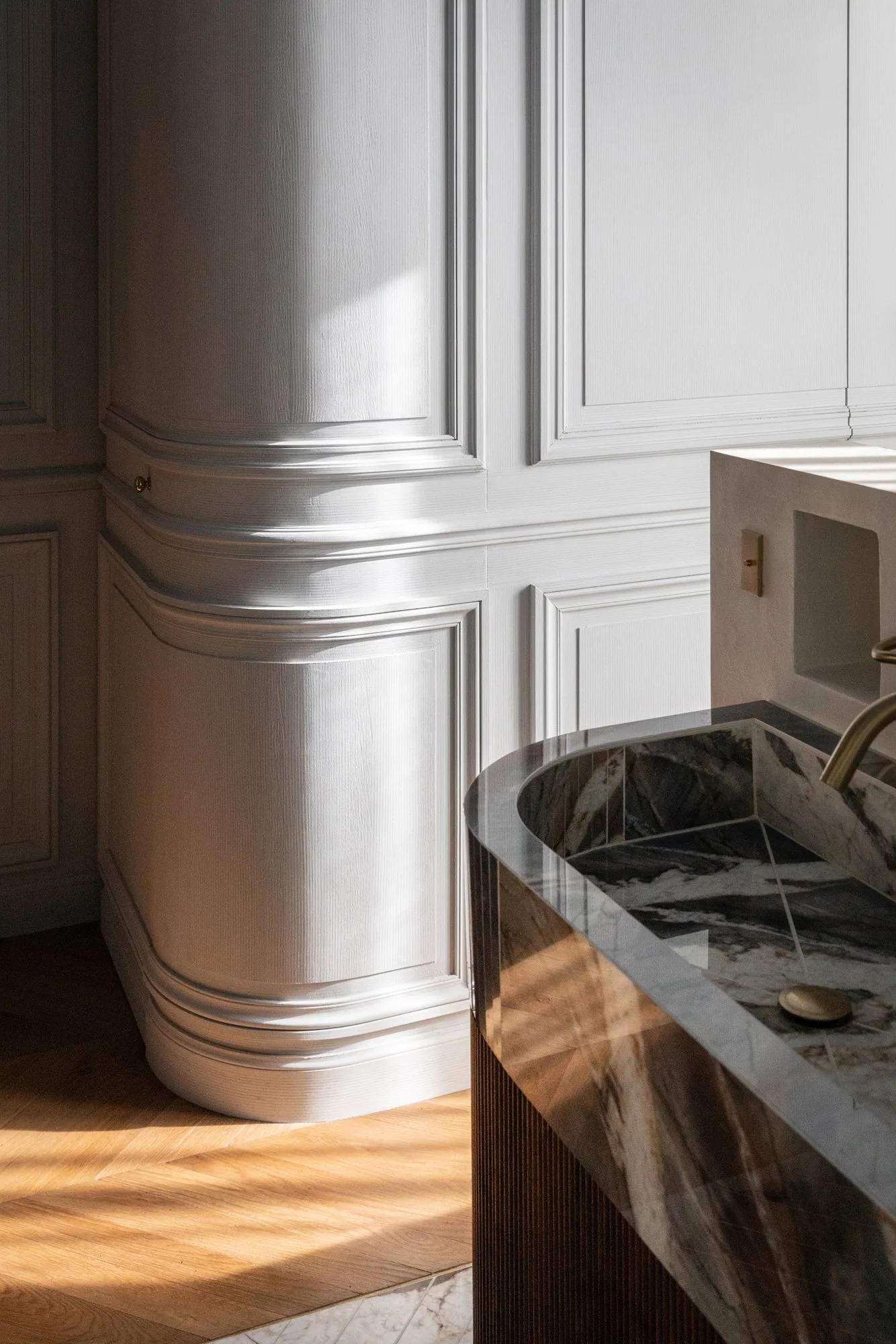 détail de boiserie courbe laqué et détail d'une cuisine en marbre et bois dans l'agencement d'un appartement parisien par l'ébéniste agenceur Lamellux