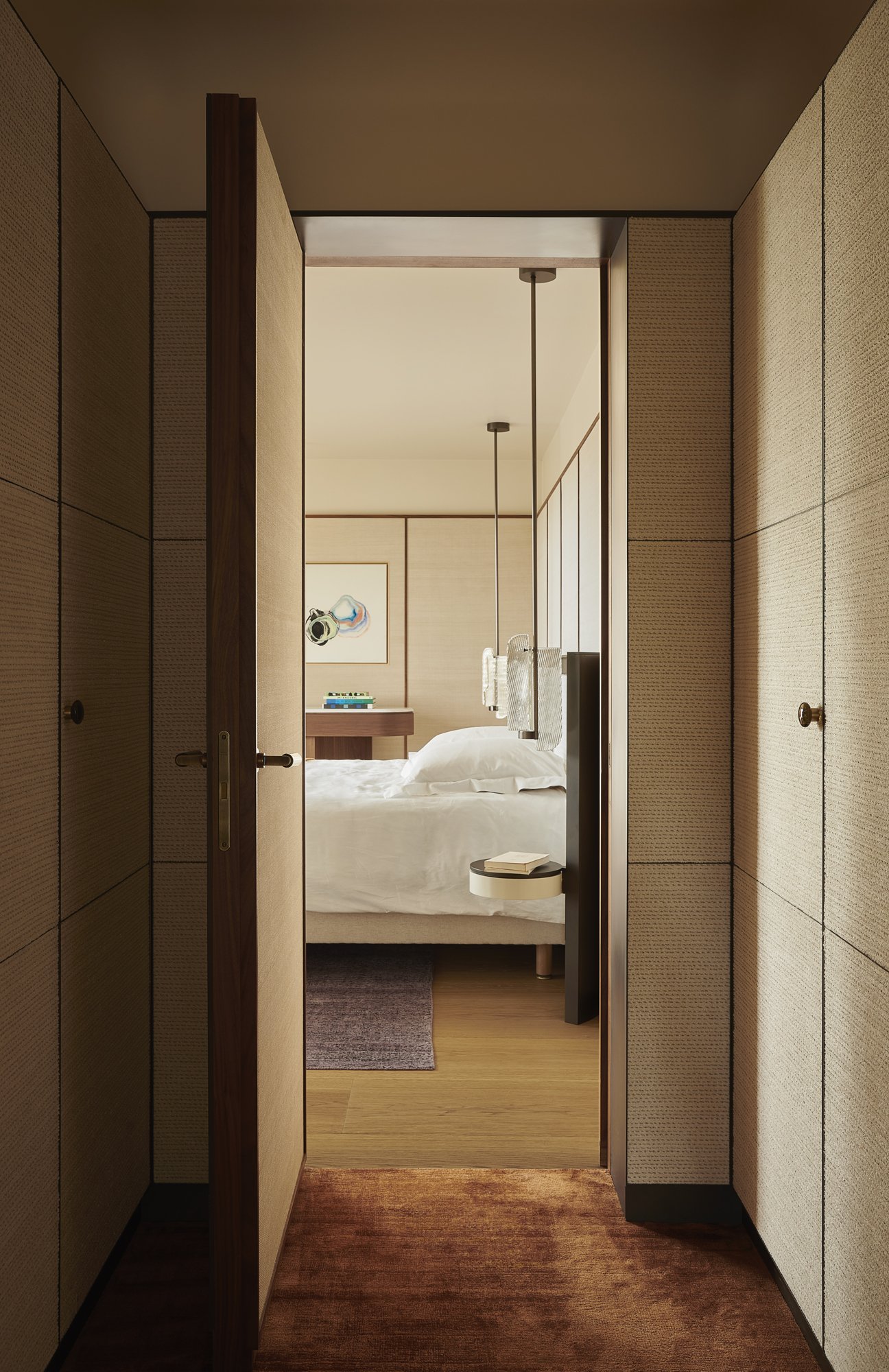 agencement dressing gainé de tissu avec portes sous tenture, cadres en laiton, vue sur chambre. réalisation par l'ébéniste agenceur Lamellux