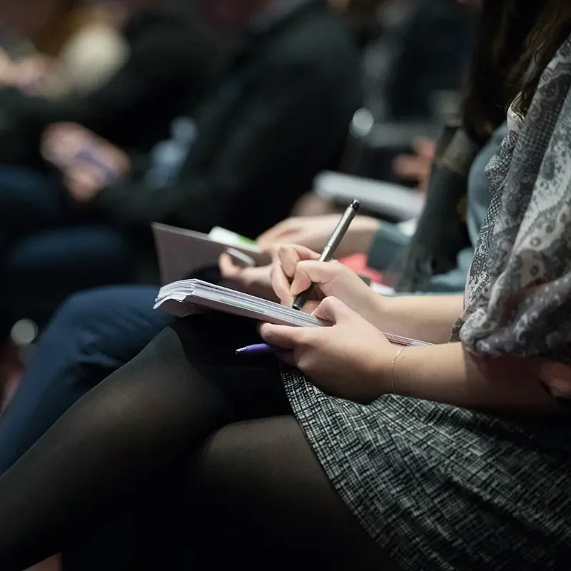a person resting their notebook on there legs, taking notes at a conference