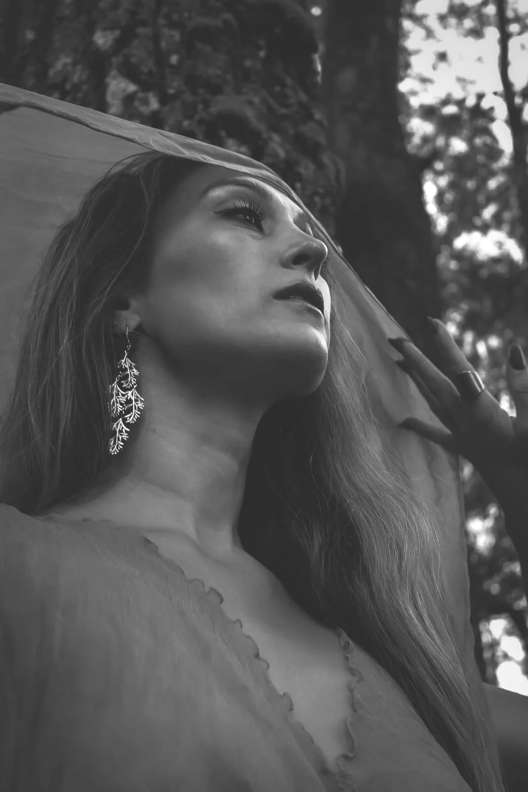 A black and white photo of a woman with long hair, wearing earrings, looking upwards under a silk scarf.