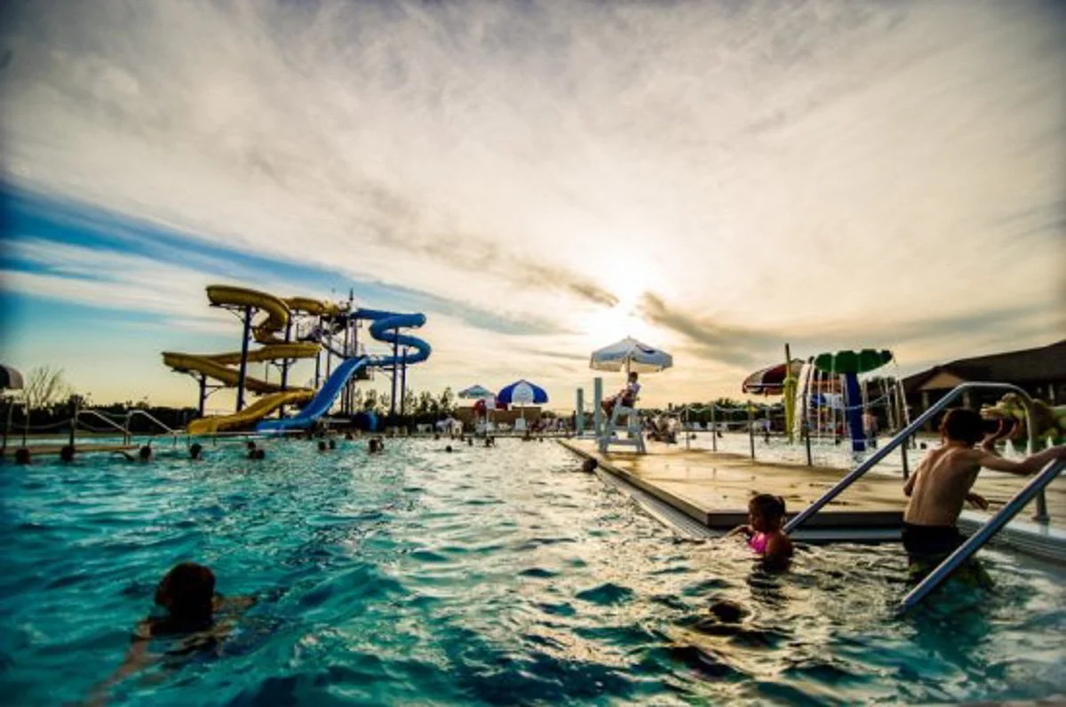 People swimming and relaxing at a water park with water slides and umbrellas during sunset.