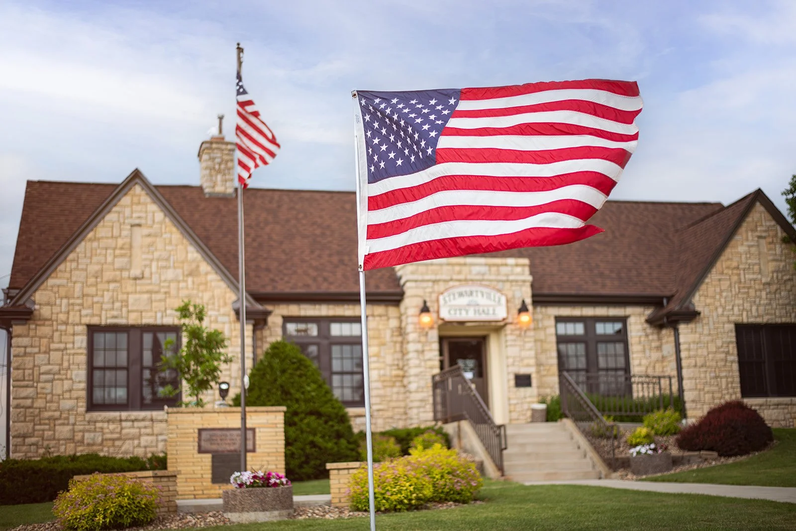 American flags outside a stone city hall building on a cloudy day.