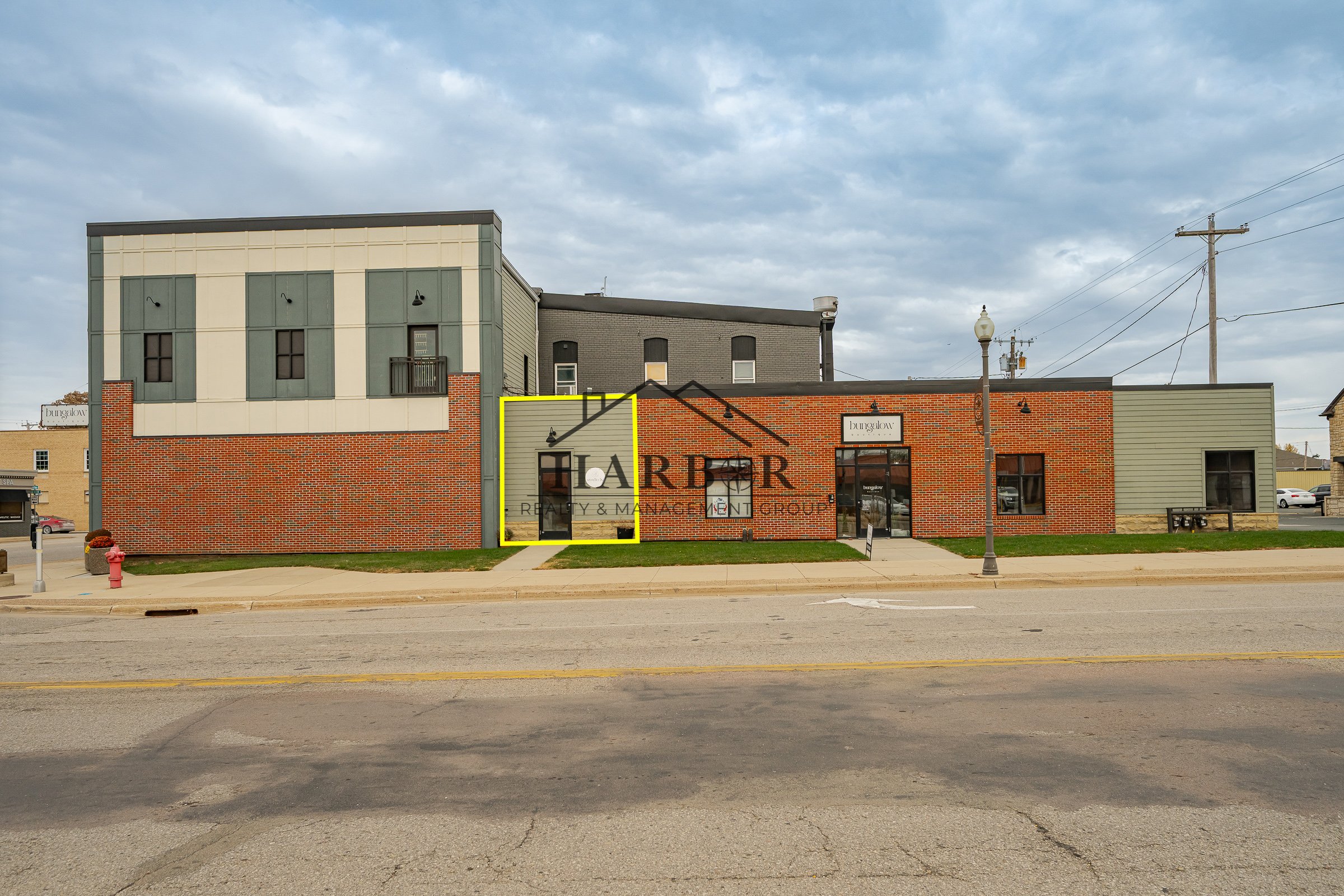 A modern commercial building with a brick facade and gray siding, situated on a sidewalk in a small town or suburban area, under an overcast sky.