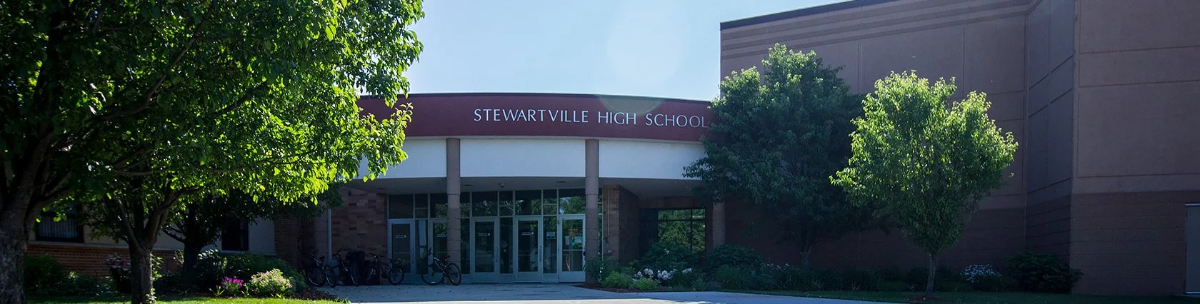 Entrance to Stewartville High School with trees and bicycles outside.