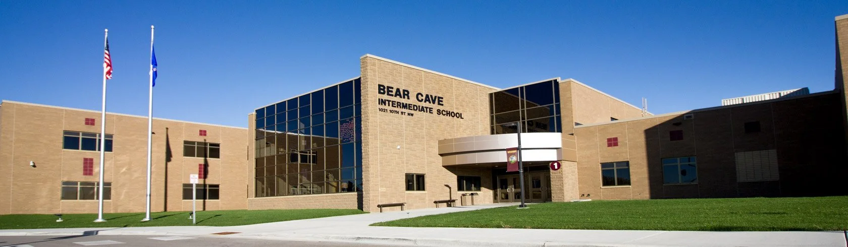 Exterior of Bear Cave Intermediate School with flags and a curved glass entrance on a sunny day.