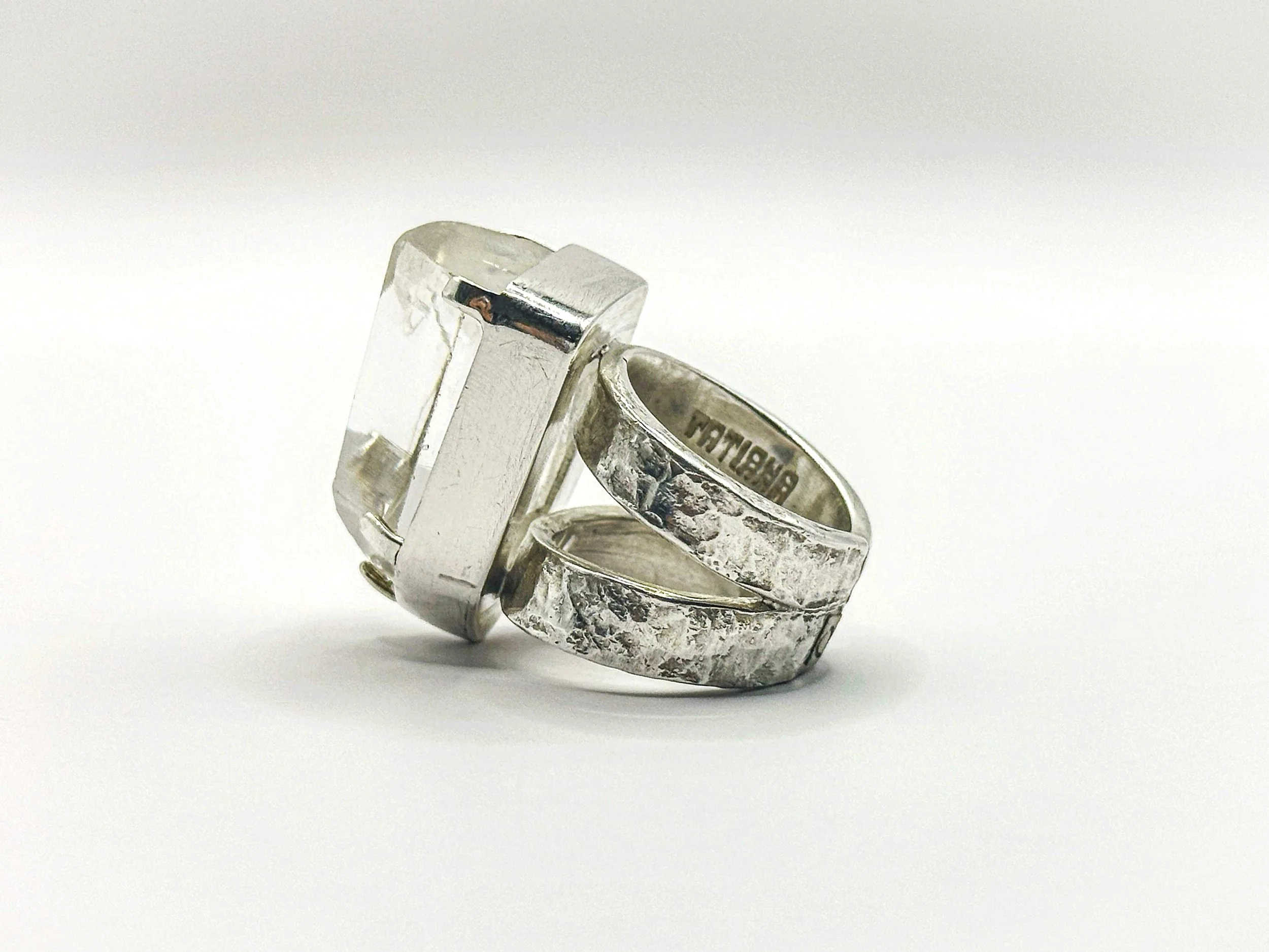 Two silver rings, one square and one textured band, positioned upright on a white surface.