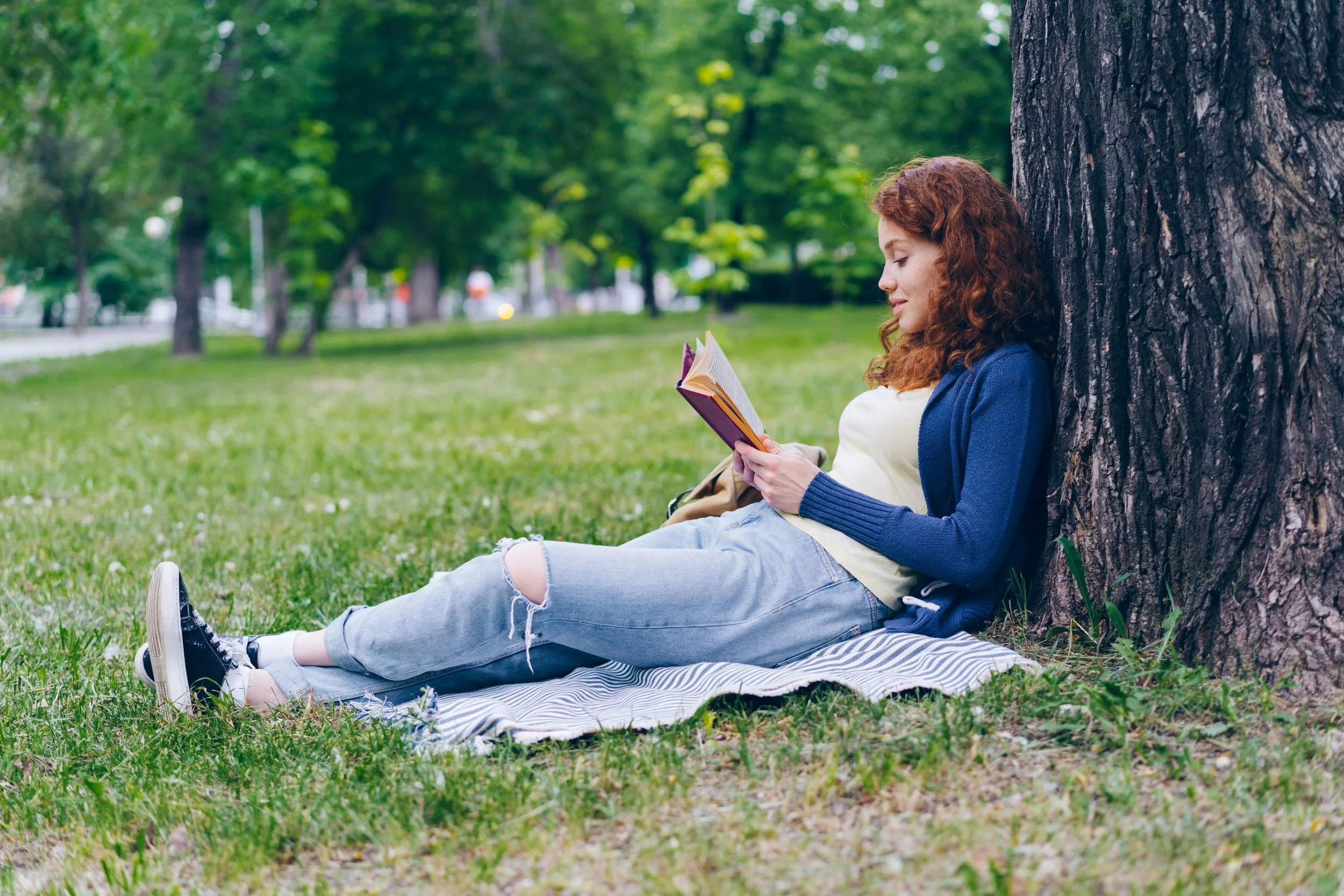 thoughtful calm young woman reading a book under a tree