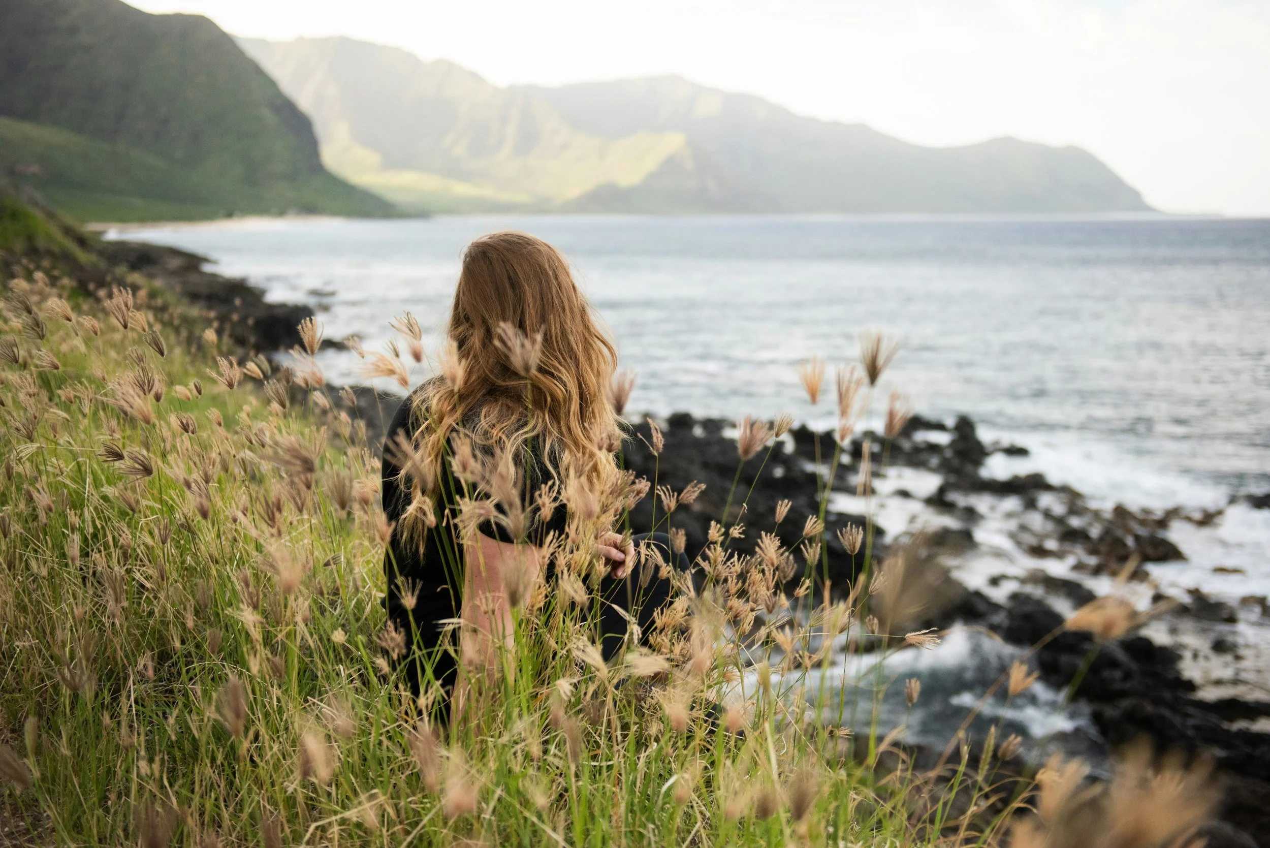 anxious young woman sitting on hillside looking at the sea