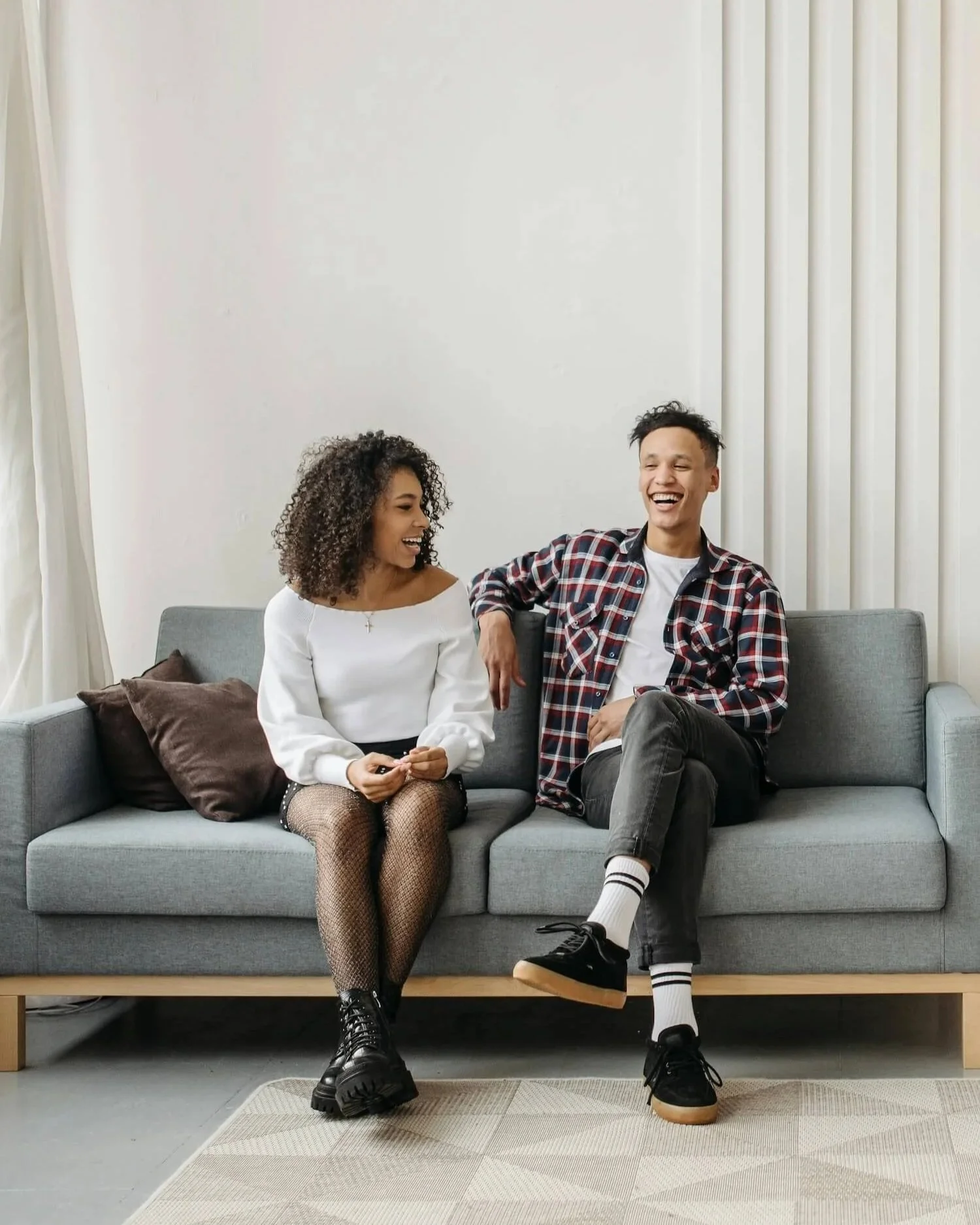 Smiling couple sitting together on a sofa, talking openly in a bright, relaxed living room.