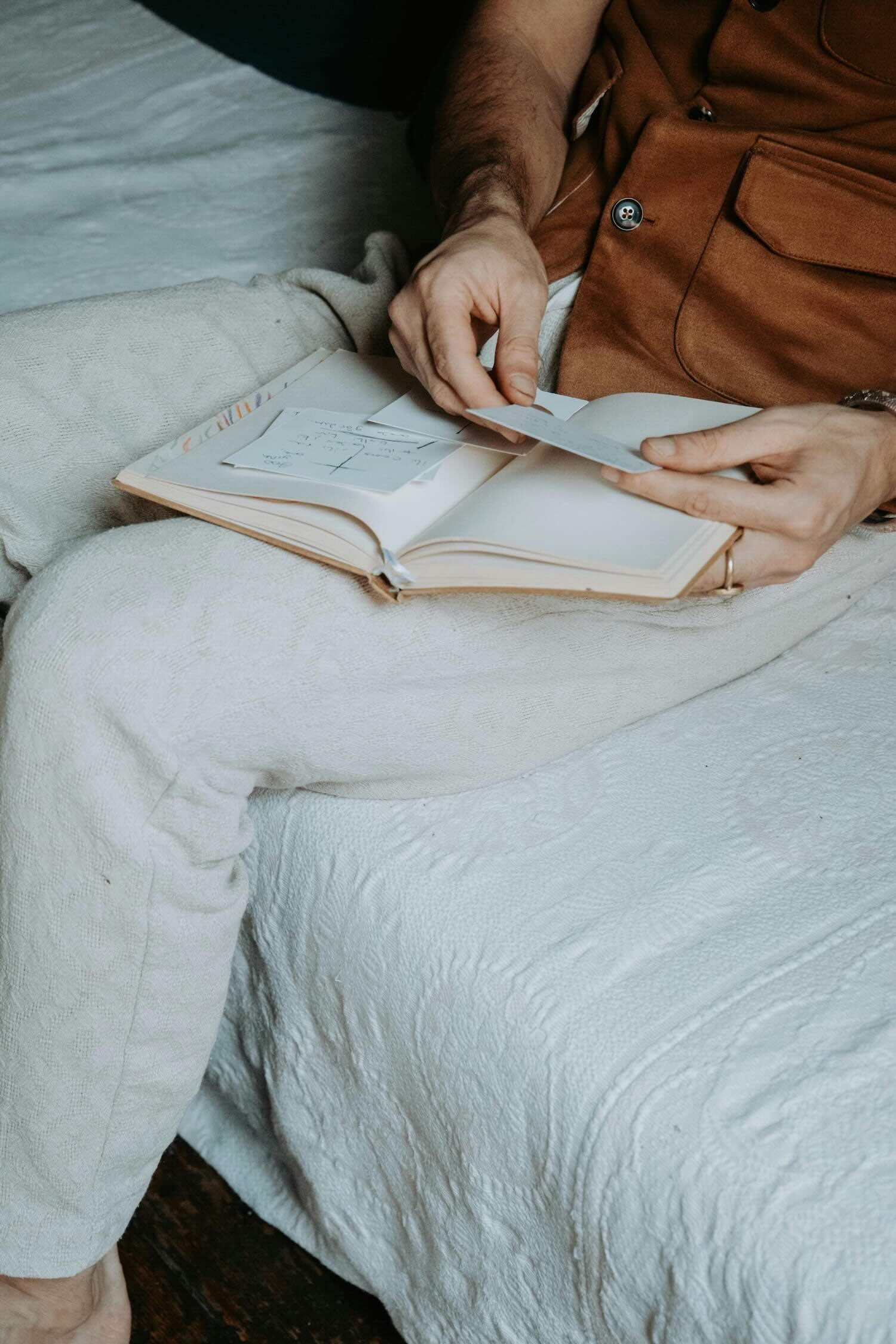 Person sitting on a bed, writing in a notebook with soft light and neutral bedding.