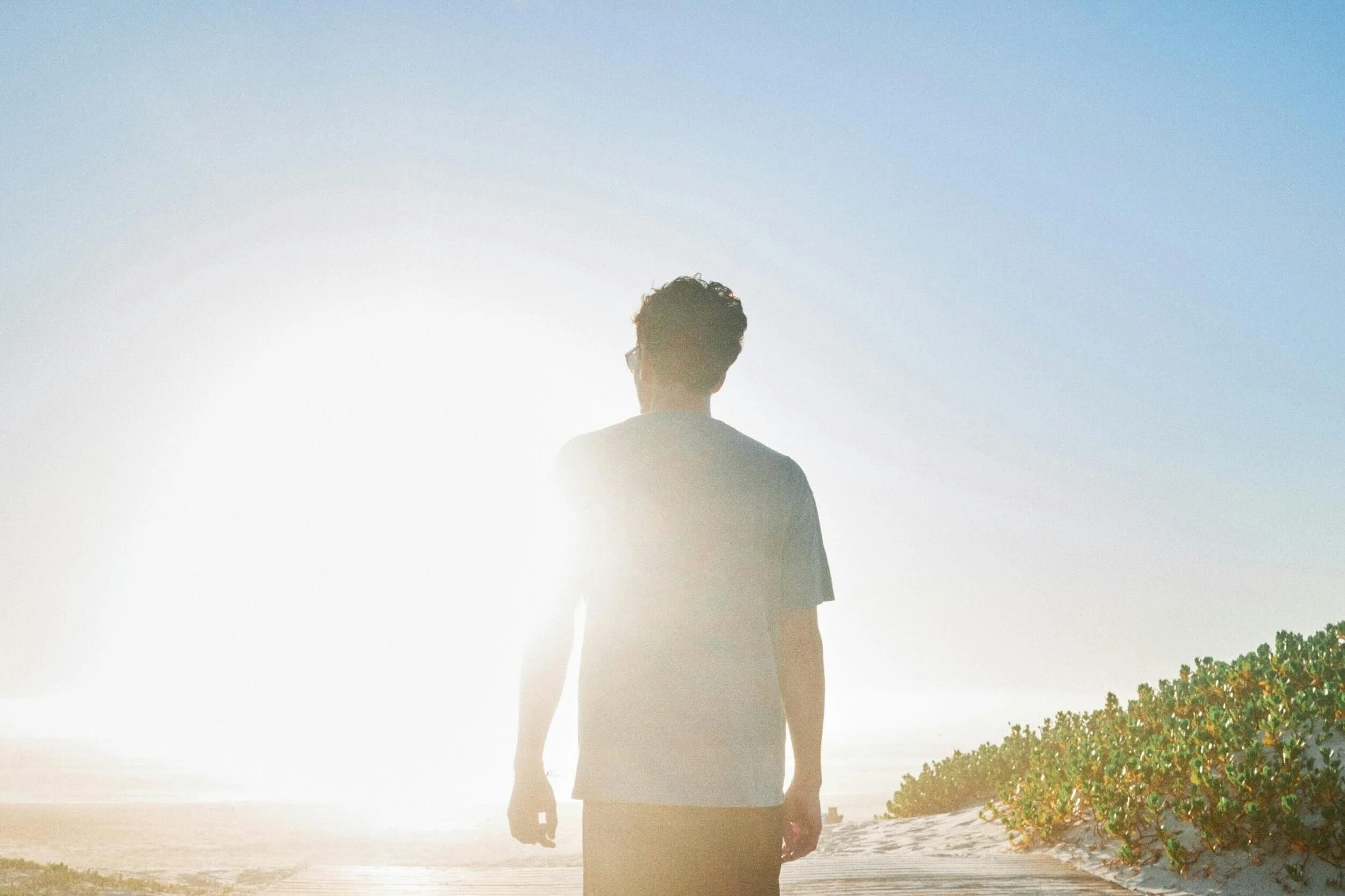 Man standing alone facing the sea in early morning light