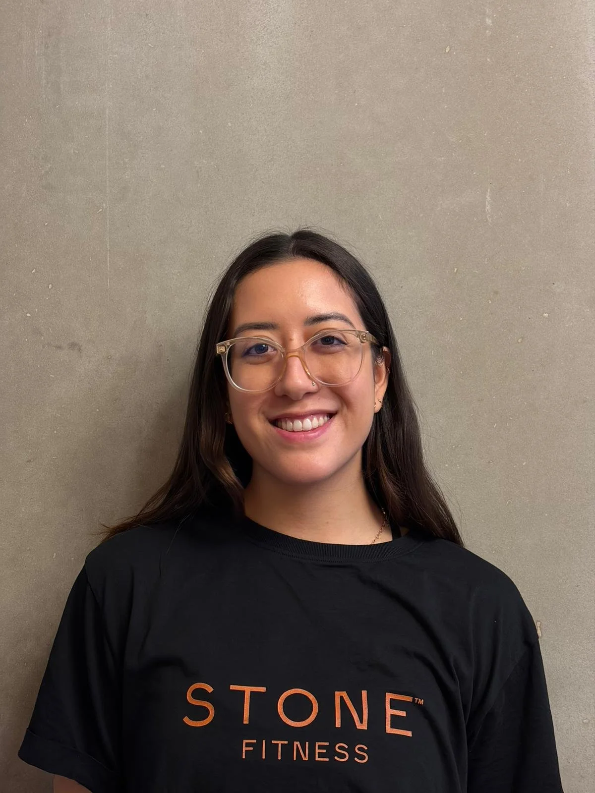 Young woman with glasses smiling in front of a white and yellow background with the word 'STONE' partially visible.