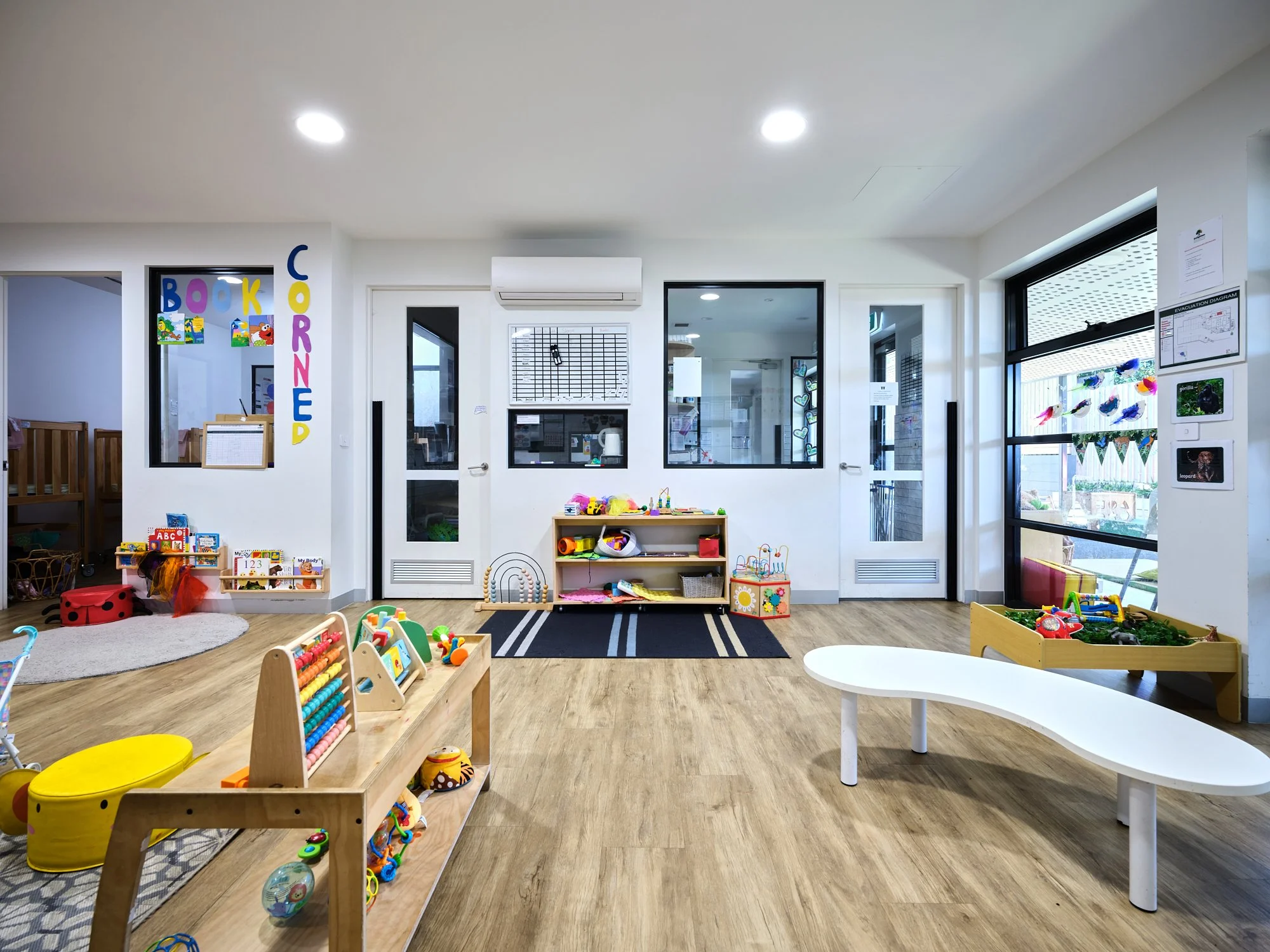 Children's playroom with toys, play structures, and colorful decorations, featuring large windows and wooden flooring.