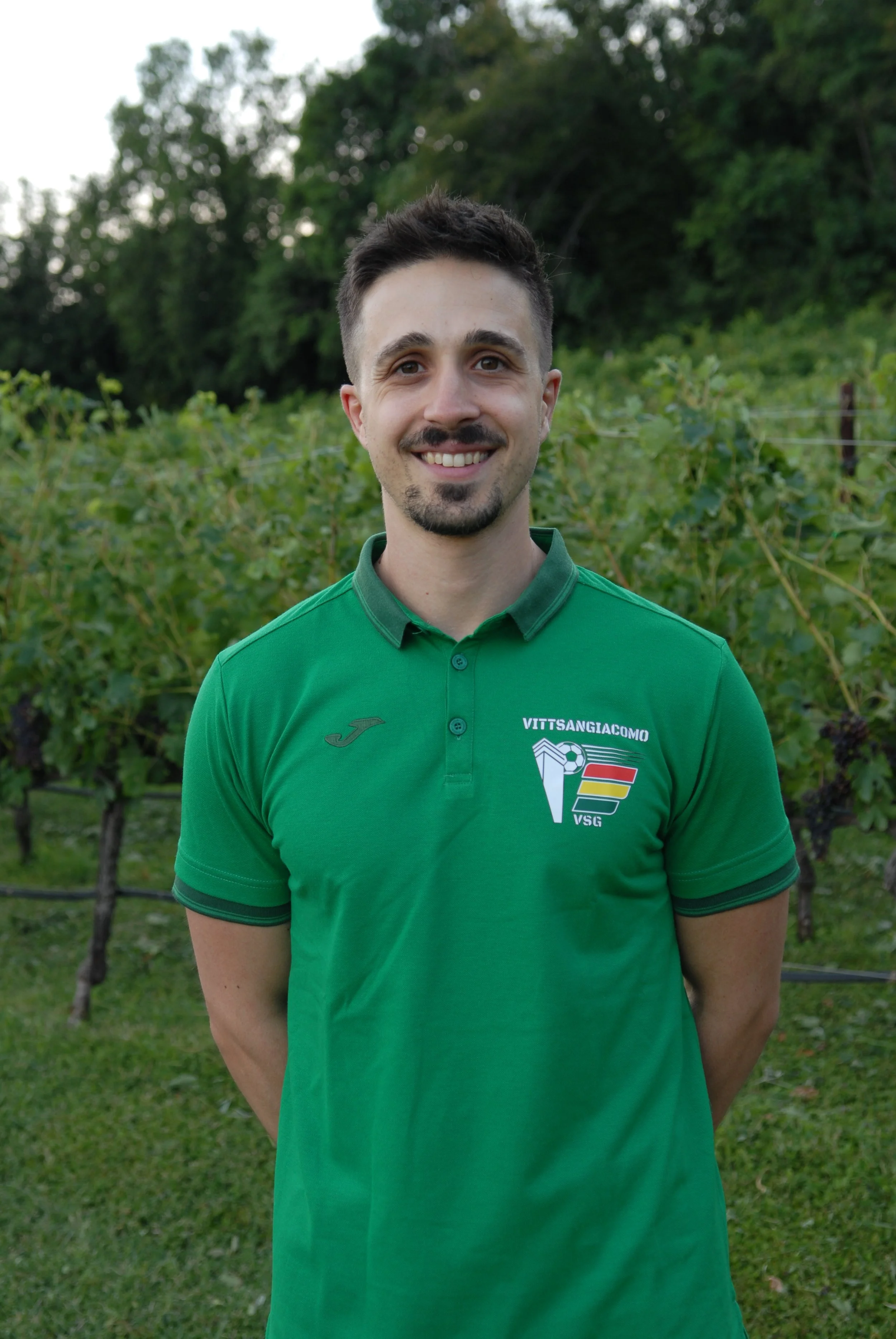 Uomo sorridente con maglietta verde davanti a una vigna.
