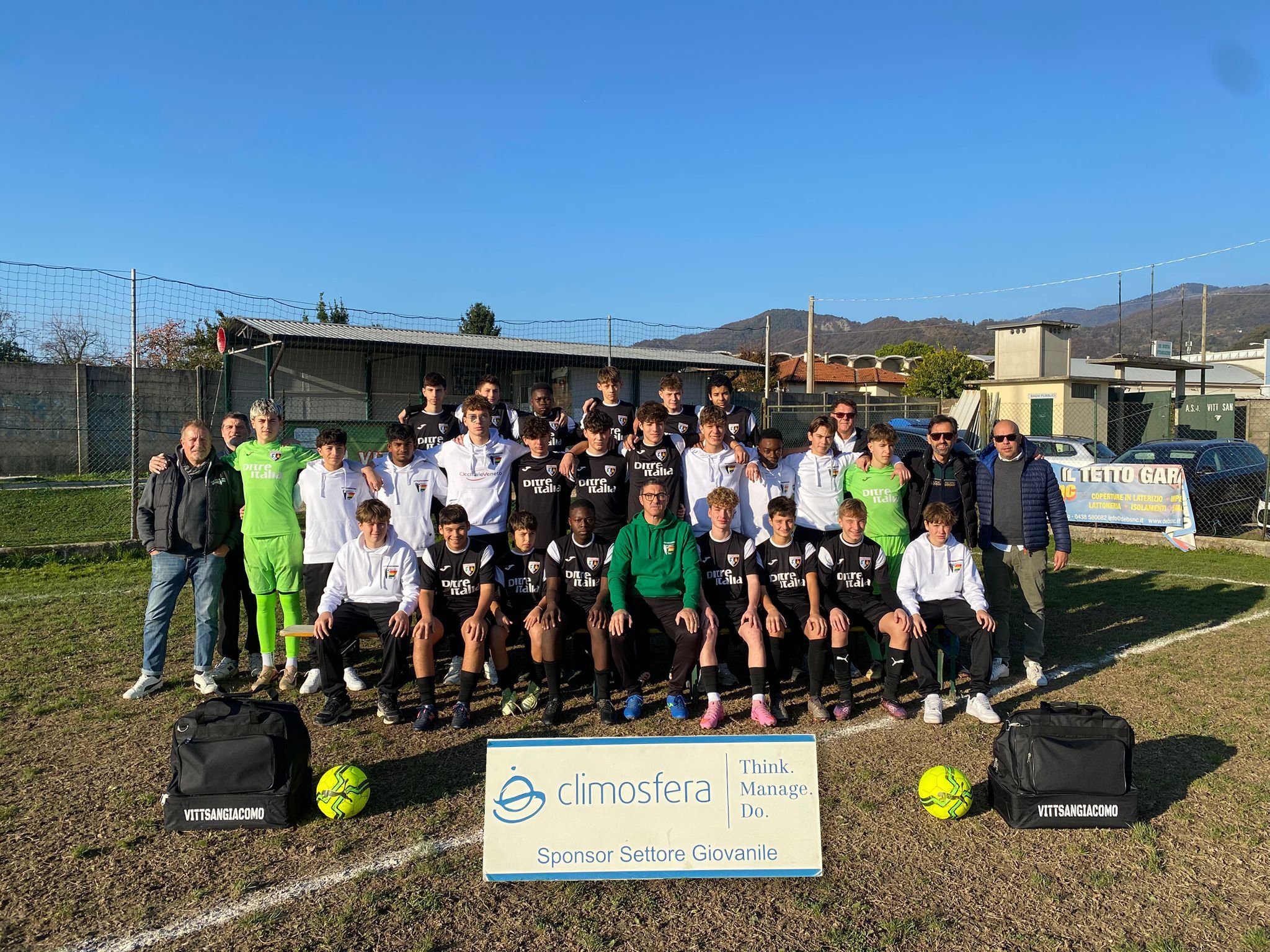 Gruppo di giovani calciatori con allenatori, posa per una foto di squadra sul campo di calcio in un giorno di sole.