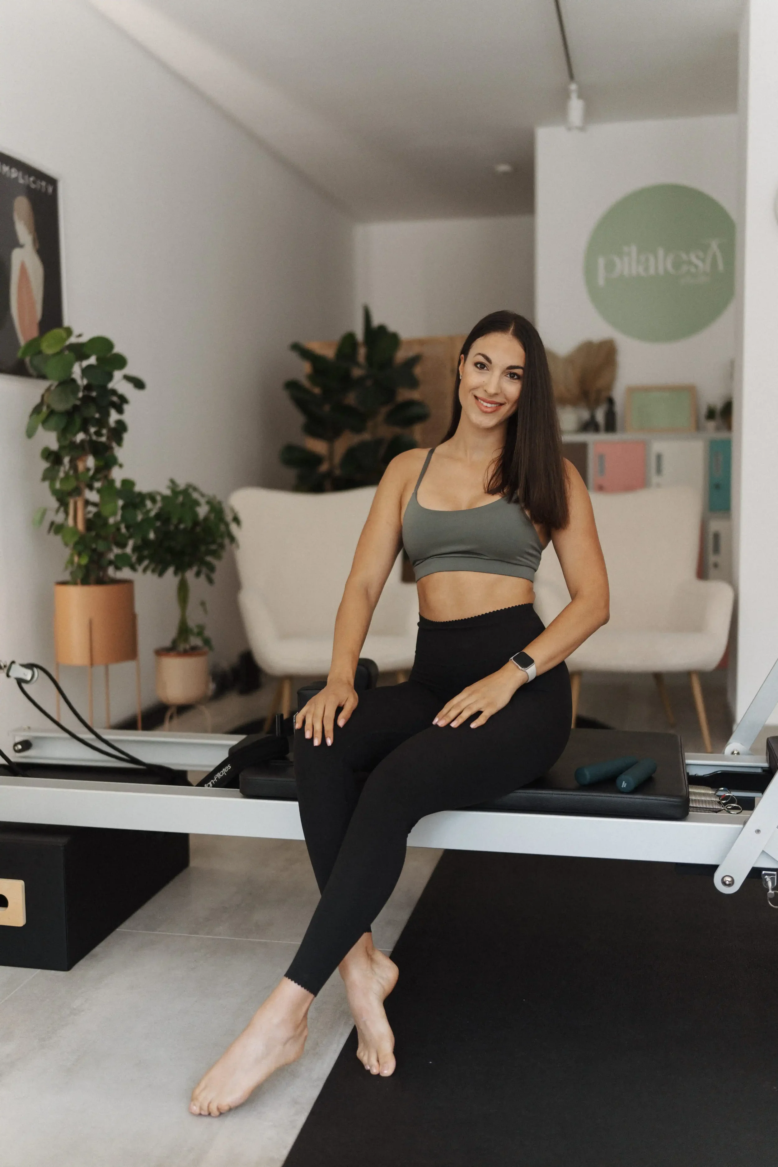 Two women practicing Pilates on reformer machines in a bright room with large windows.