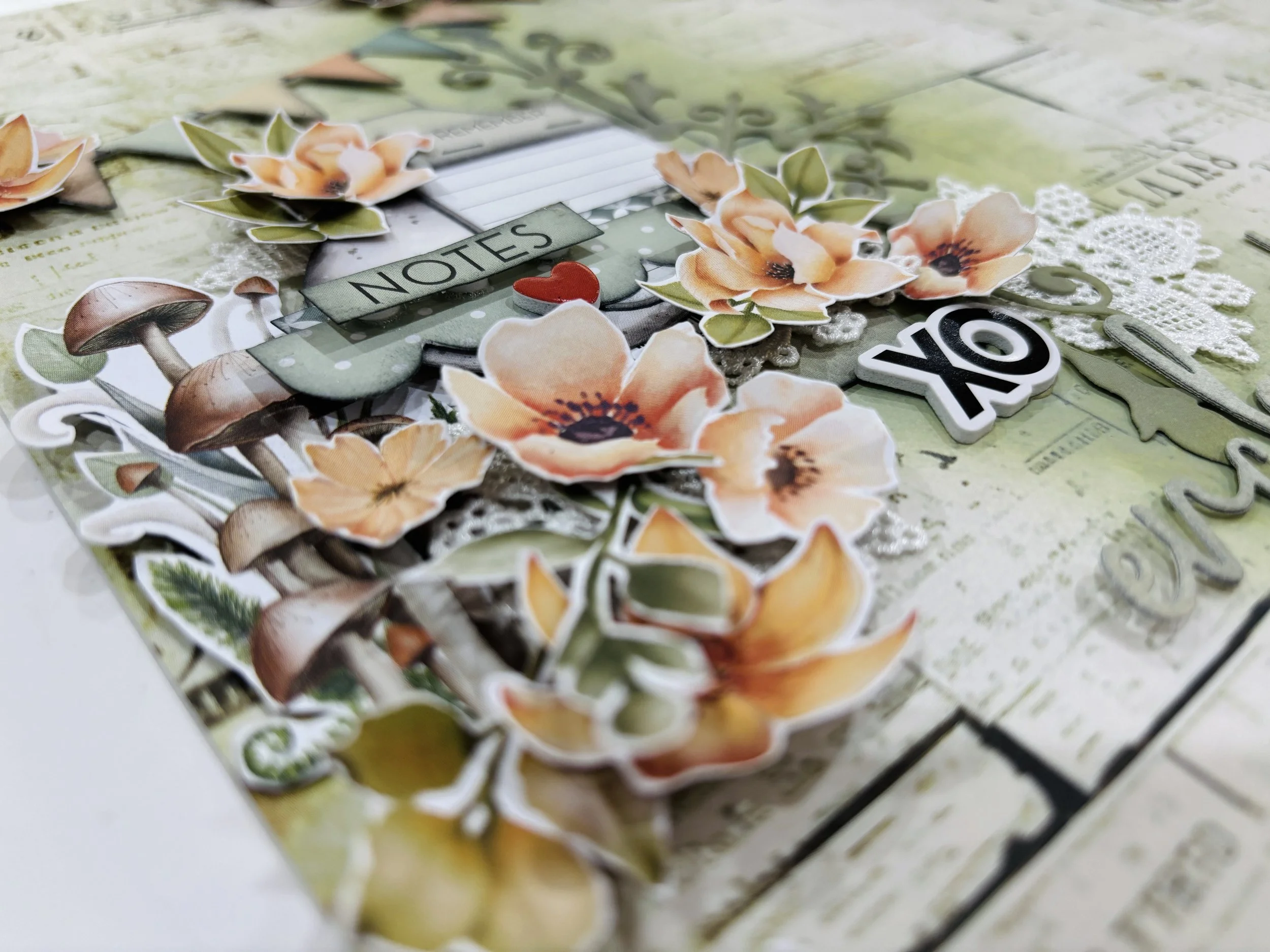Close-up of a scrapbook page with floral stickers, paper cutouts, and decorative elements, including the word "NOTES" and the phrase "OK".