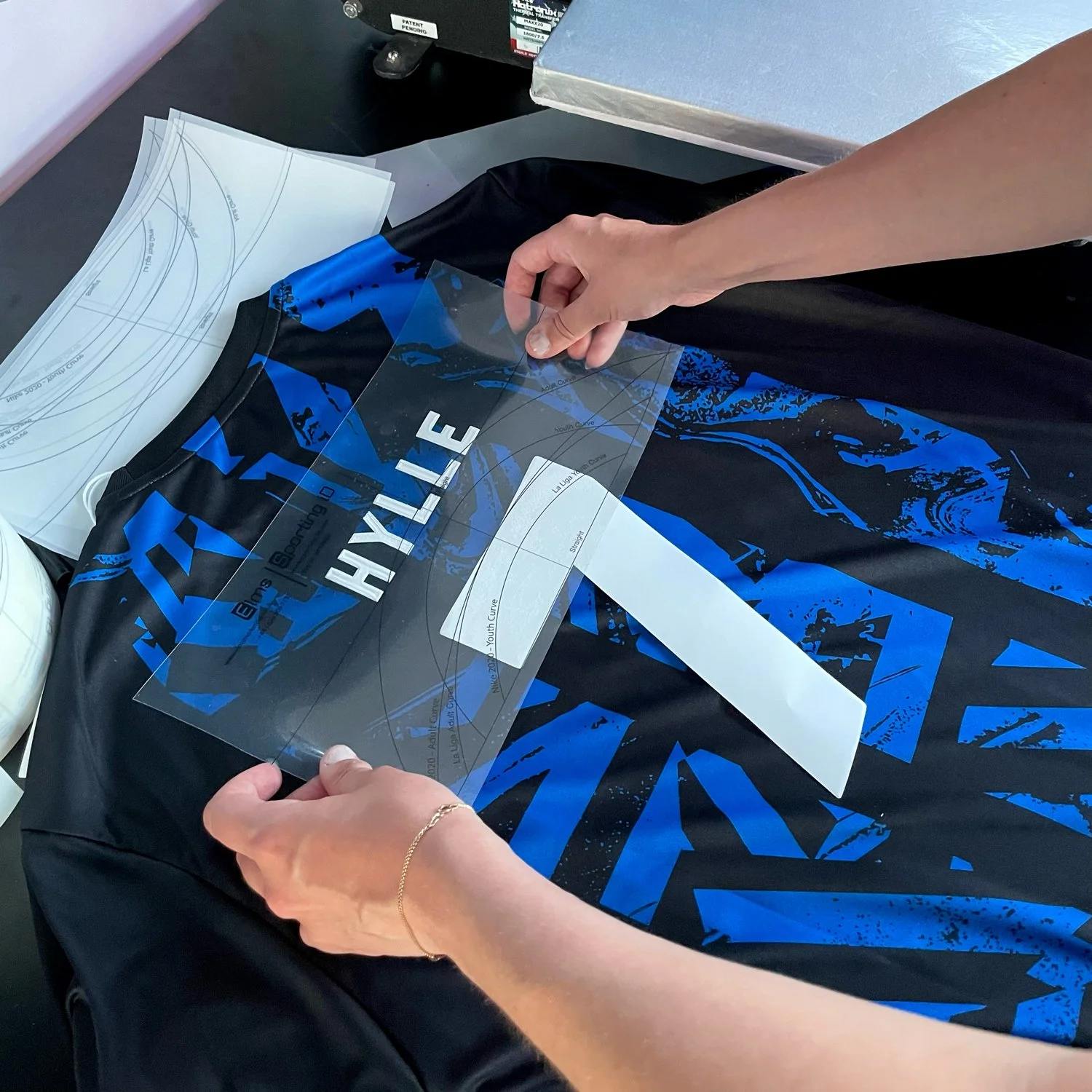 Person placing a clear adhesive sports jersey nameplate on a black and blue athletic jersey during customization.