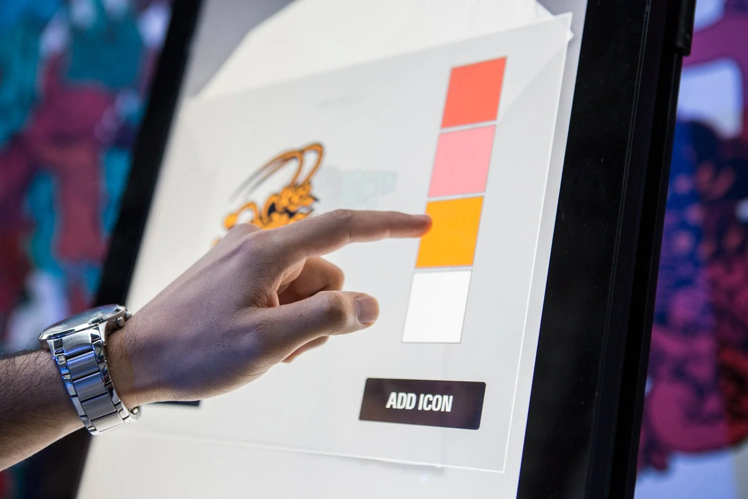 Person selecting a orange-colored option on a digital interface screen with a logo and color palette, wearing a silver watch on their wrist.