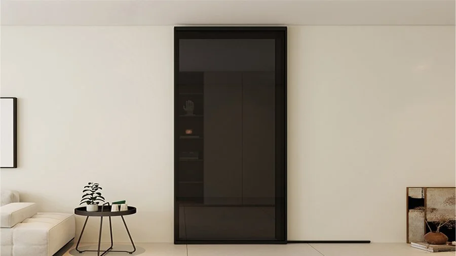 Minimalist living room with a black enclosed cabinet, a white sofa, a round black side table with a plant and small objects, and a partially visible artwork on the floor.