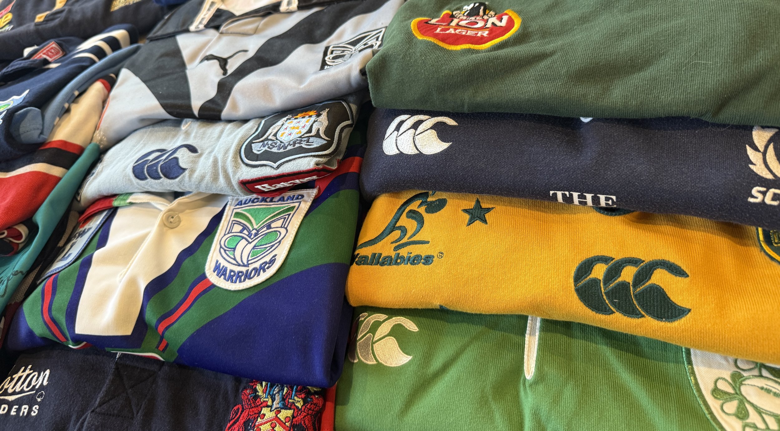 Stacks of vintage rugby jerseys including All Blacks, Wallabies and European teams