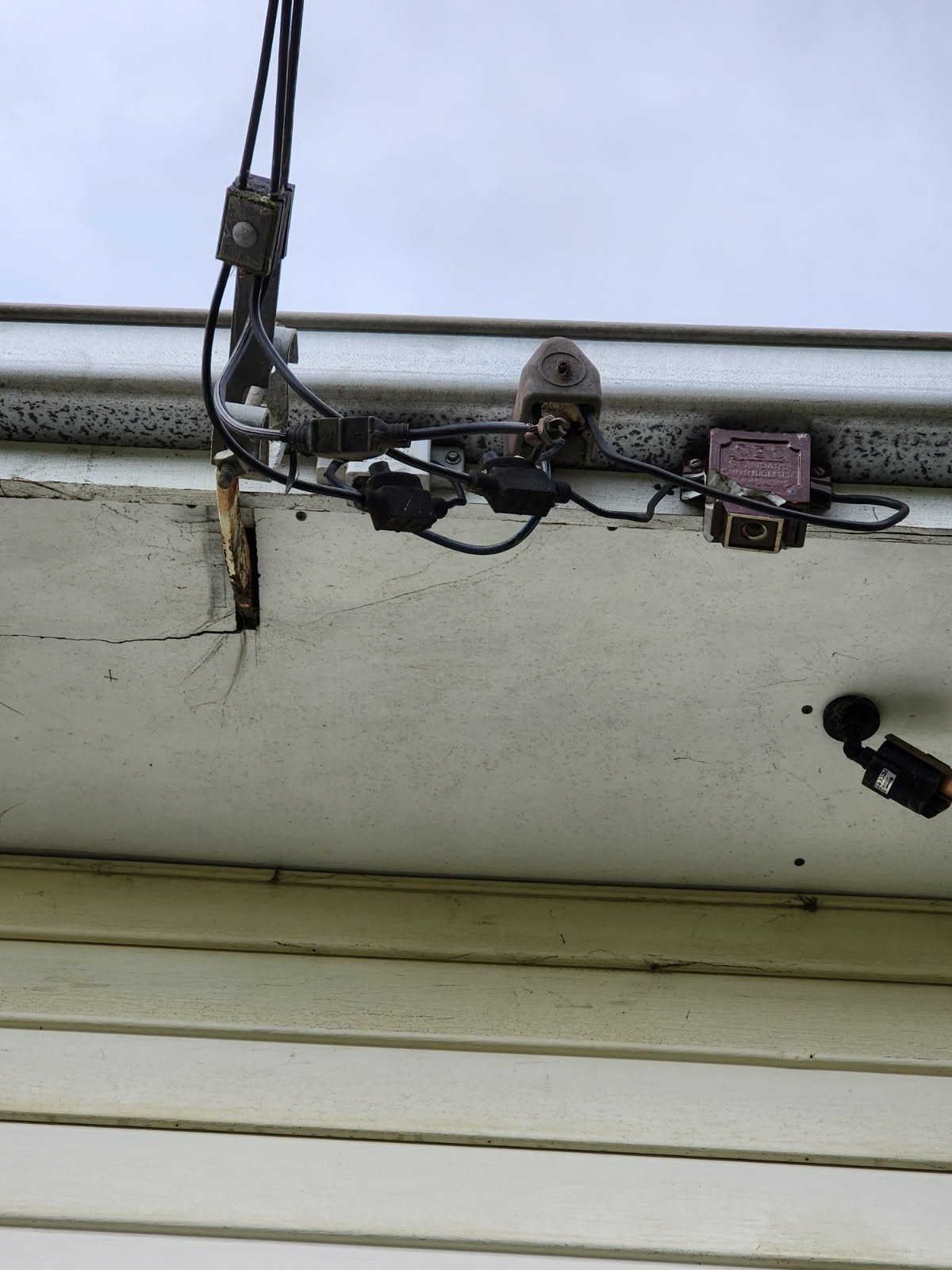 Close-up of damaged and disconnected wires and cable connectors on the exterior of a building near a garage door.
