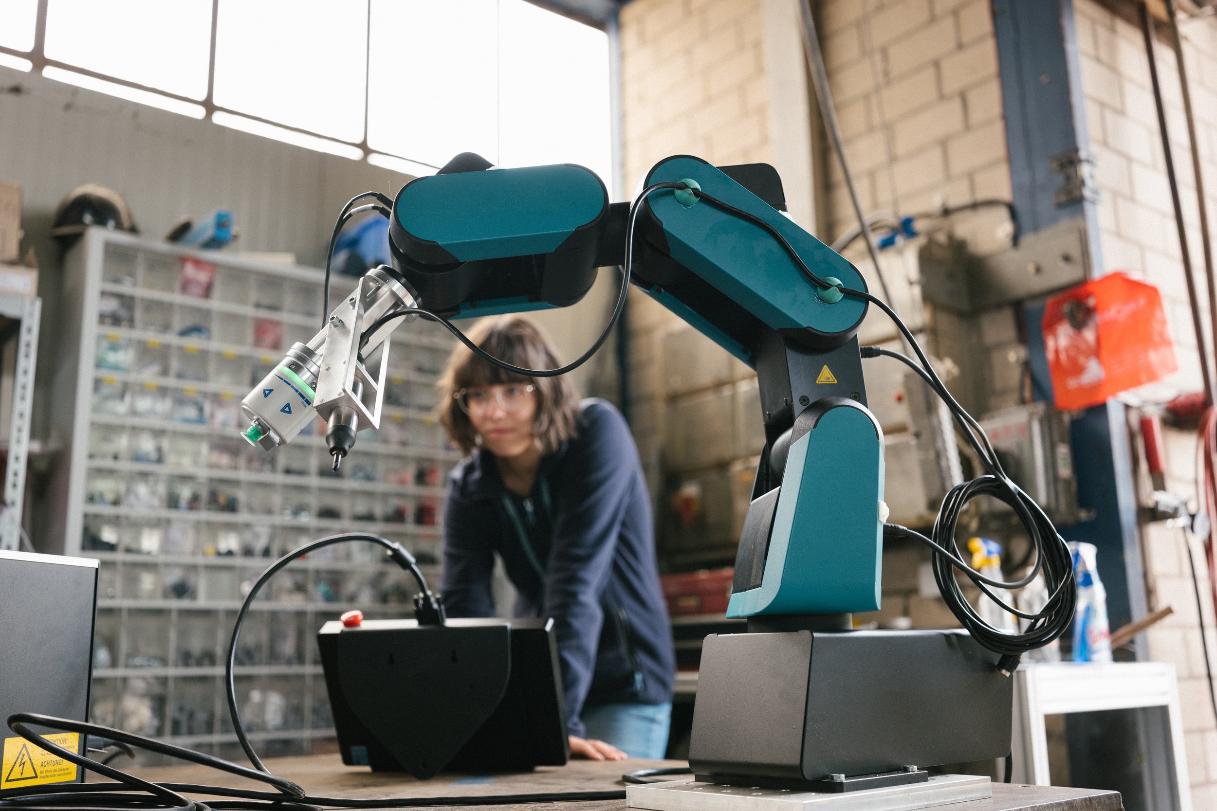 Robotic arm in an engineering workshop with a technician working in the background.