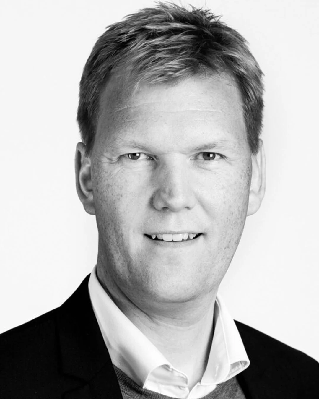 Sort-hvid portrætfoto af en mand i formel påklædning, smilende.