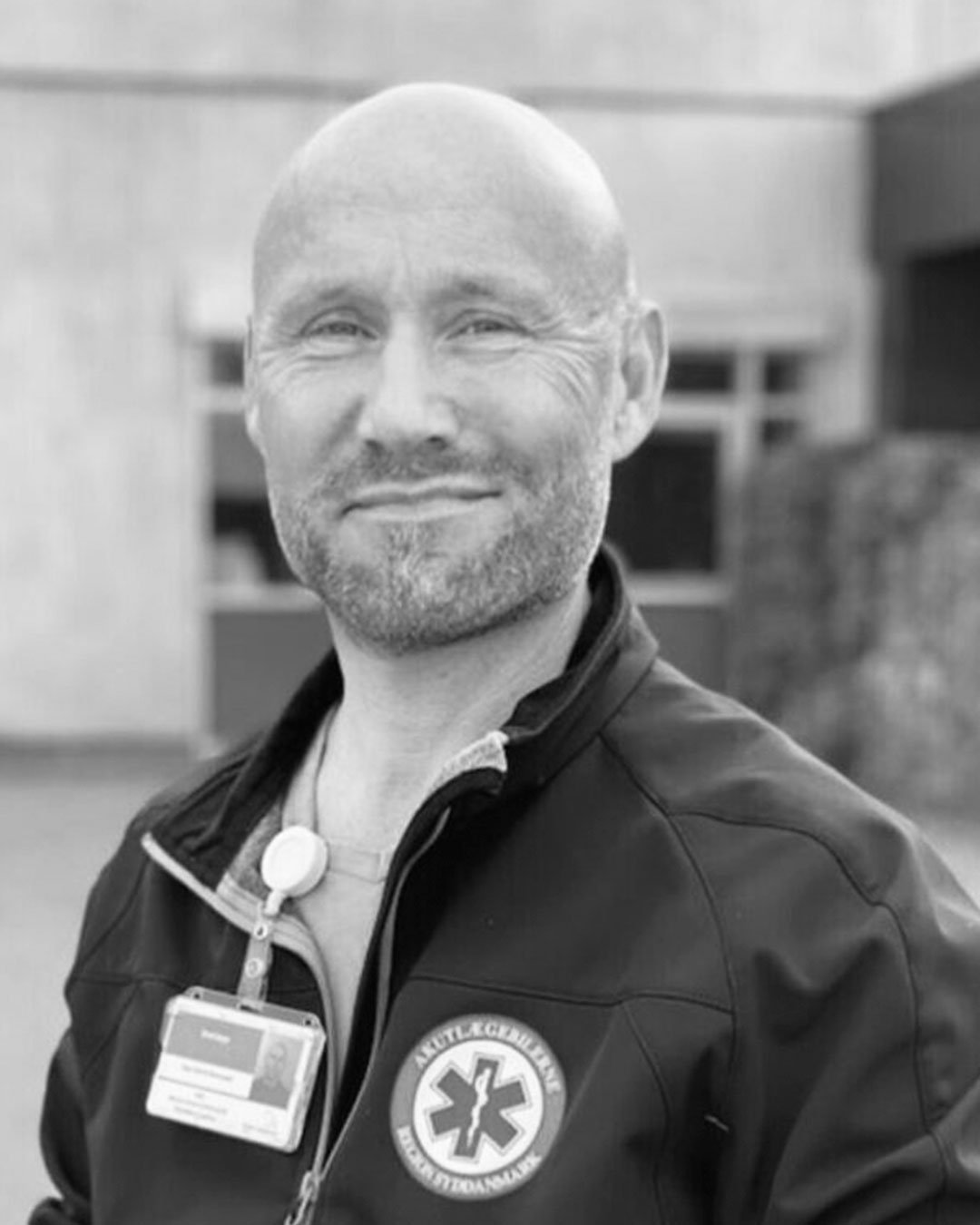 Mand i ambulanceuniform med badge, smilende, udendørs.
