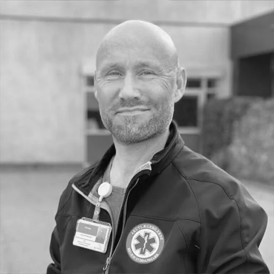 Mand i ambulanceuniform med ID-badge foran en bygning