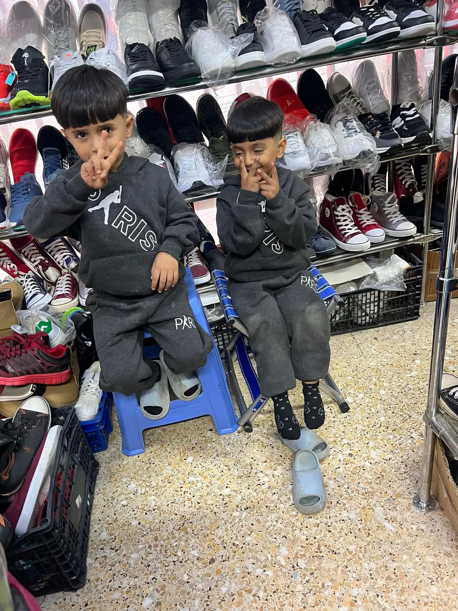 To unge drenge sidder i en hink i en butik, omgivet af sko på hylder. De smilede og lavede peace-tegn til kameraet.