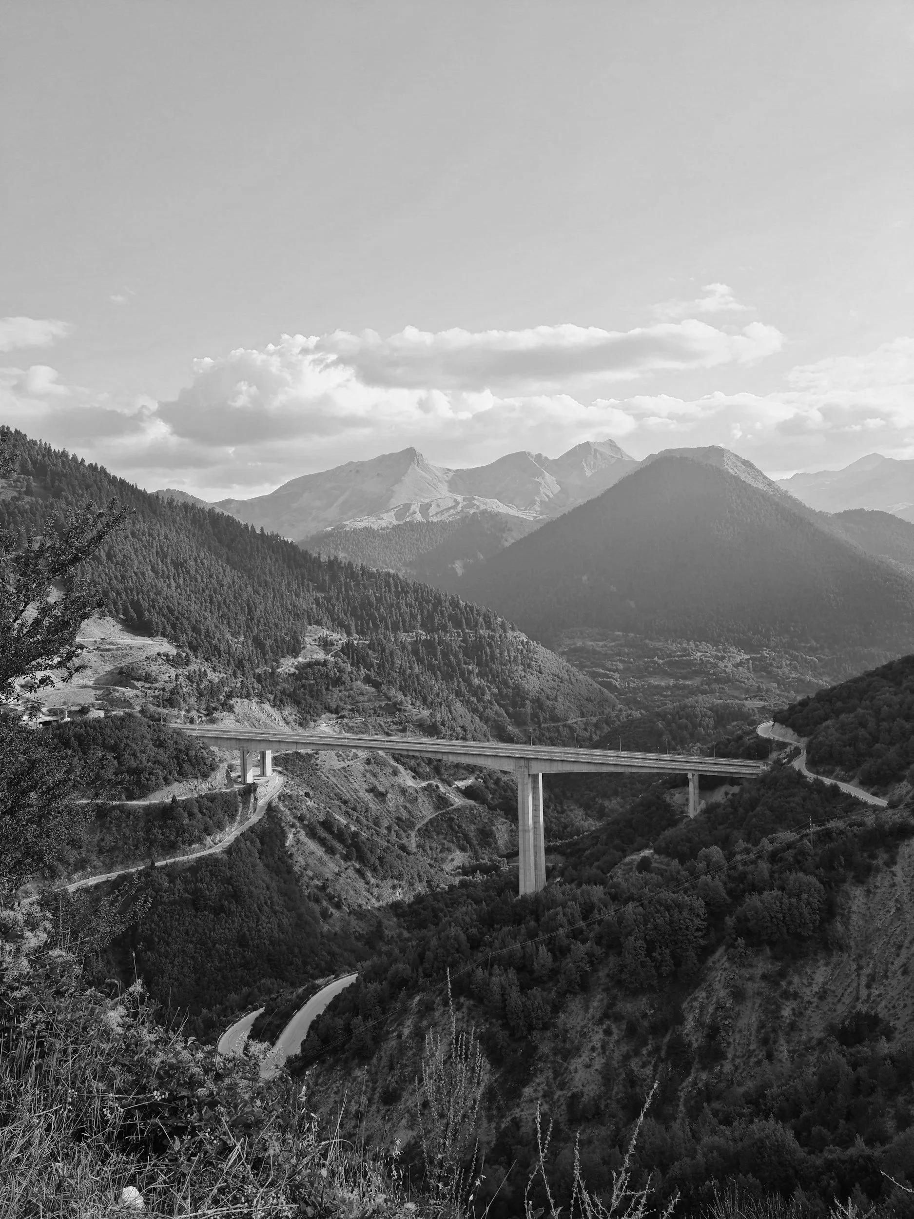 Paesaggio montano con una strada che attraversa il ponte su una valle: vista panoramica di montagne e cielo con nuvole.