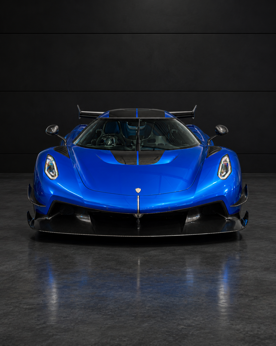 A blue sports car with black aerodynamic accents and a rear spoiler, parked against a black wall.