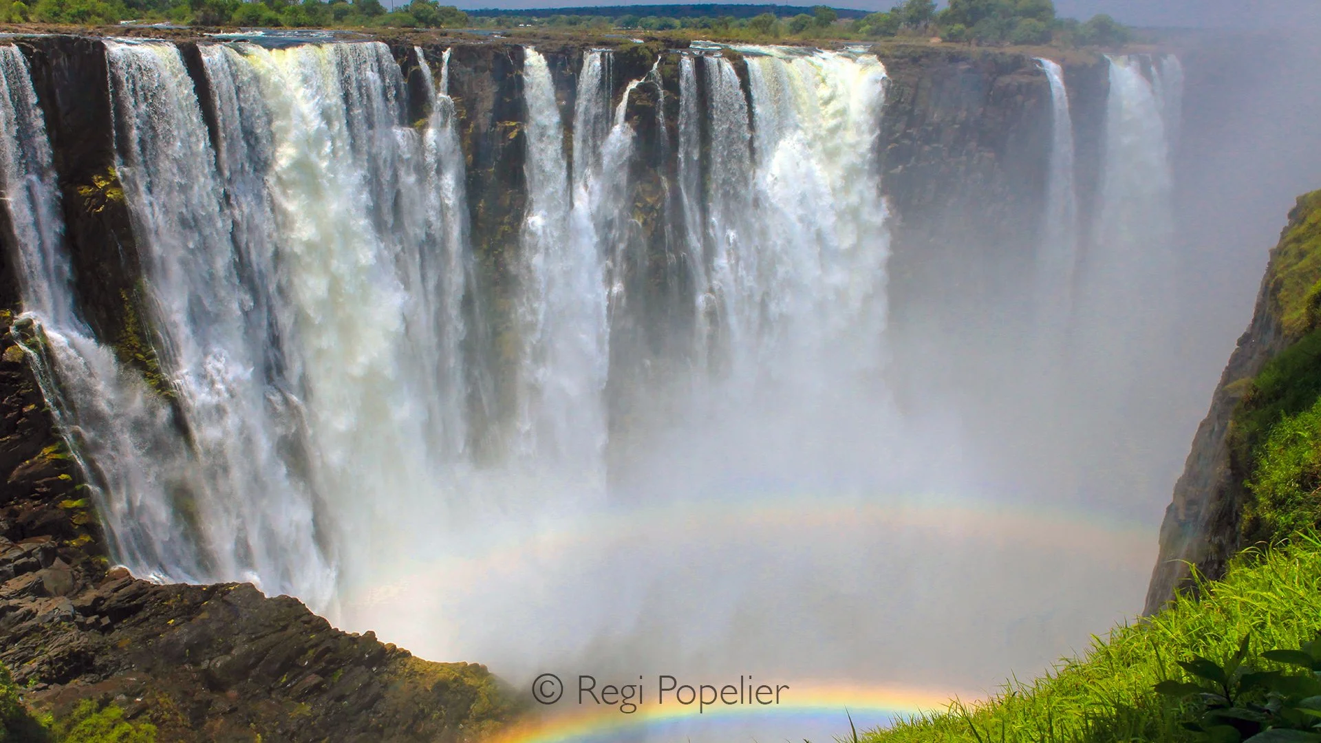 ZIM024 - A rainbow dances in the mist of Victoria Falls, painting the roar of the waters with color.