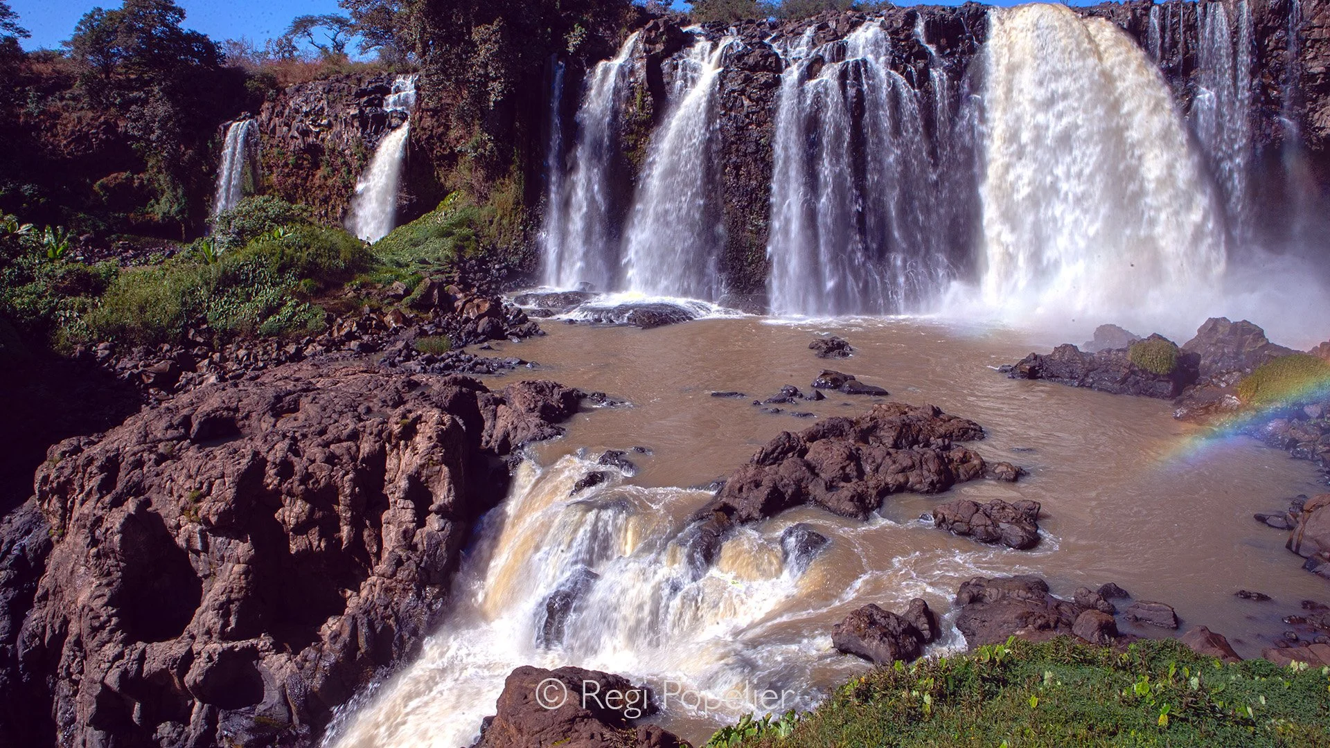 ETH056 - From a photographic point of view, the Blue Nile Waterfalls offer dramatic motion, misty atmosphere, and powerful contrasts, rushing white water against dark basalt cliffs, framed by rainbows, lush greenery, and ever changing light that make