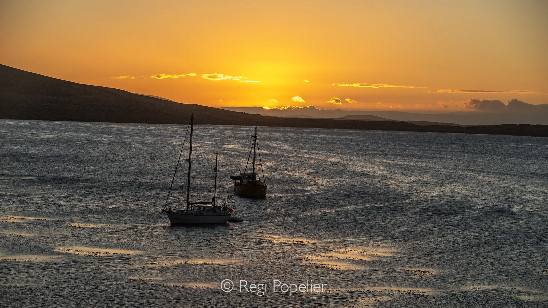 FAL007 - Bleaker Island at sunset, where boats drift in tranquil waters.