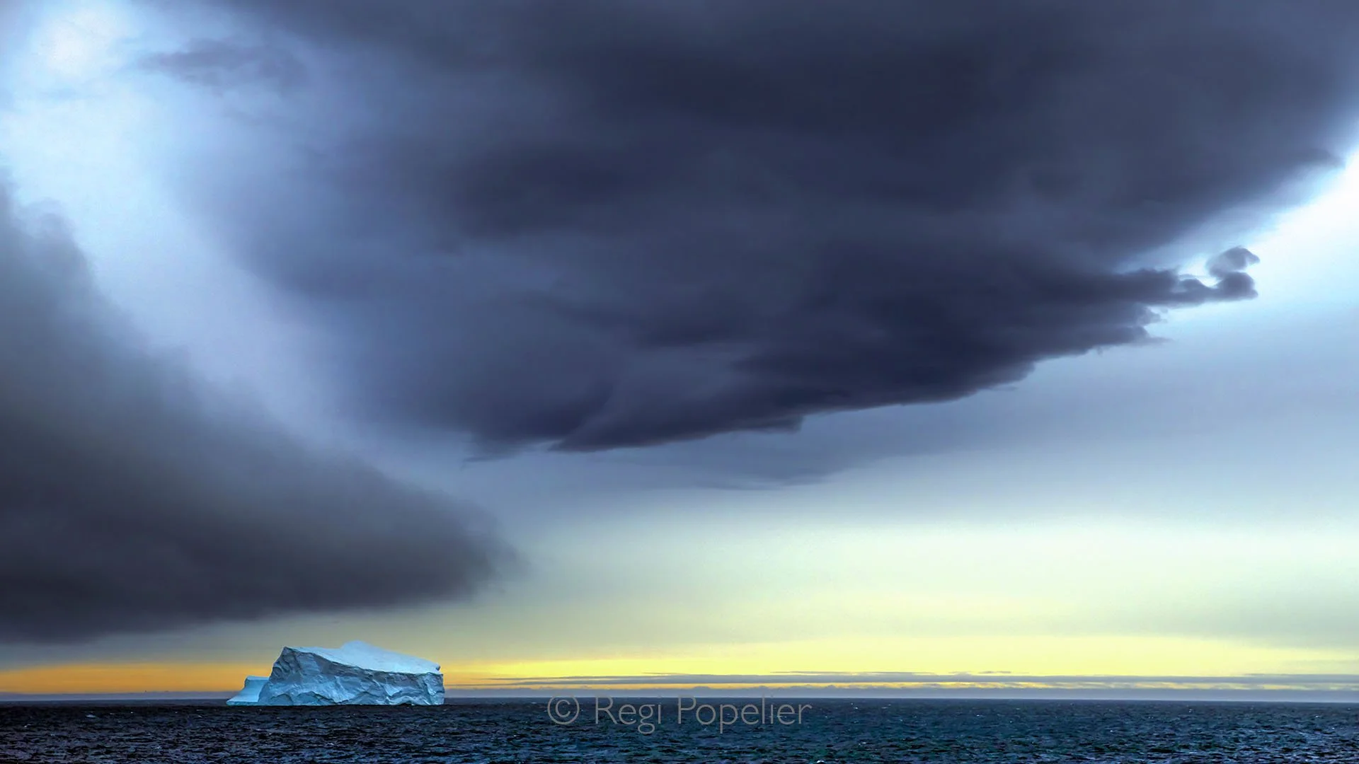 ANT012 - An iceberg drifts away from the glacier at evening,  wide ocean and moody clouds setting a dramatic scene in the polar wilderness.
