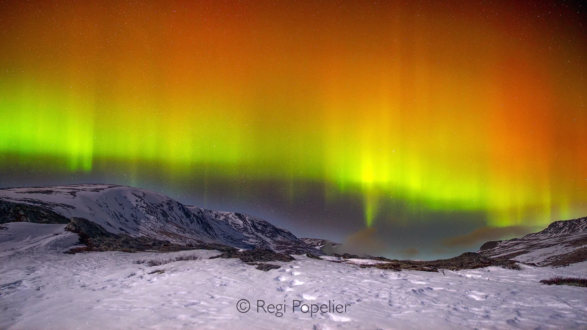 NORWAY060 - Waves of emerald light ripple above snow covered mountains, revealing the magic of an Arctic night where earth, stars, and the Northern Lights come together in perfect harmony.