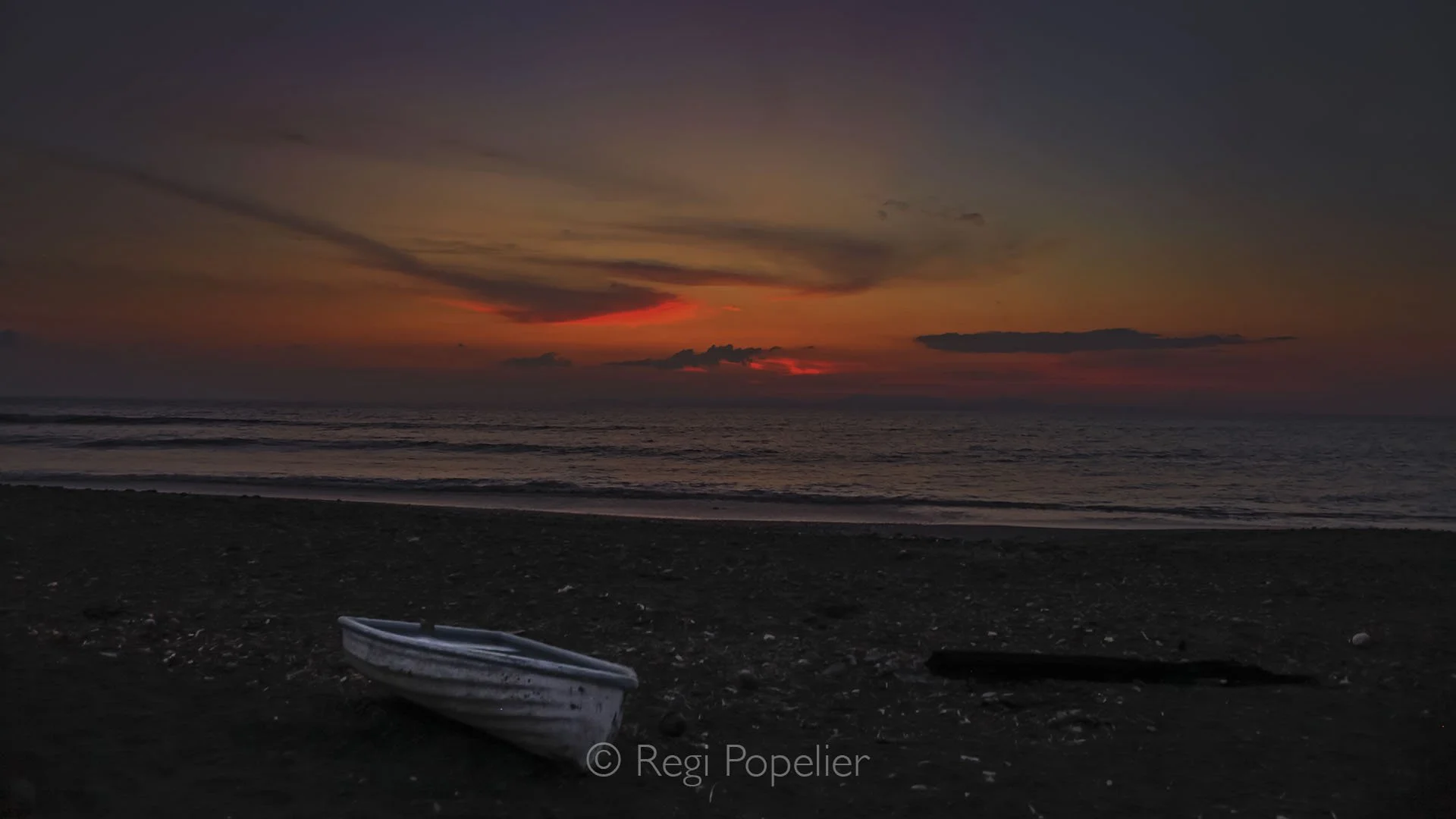CR019 - A small boat is silhouetted against the fiery hues of the setting sun, its dark outline drifting peacefully as the sky glows in deep reds and oranges.