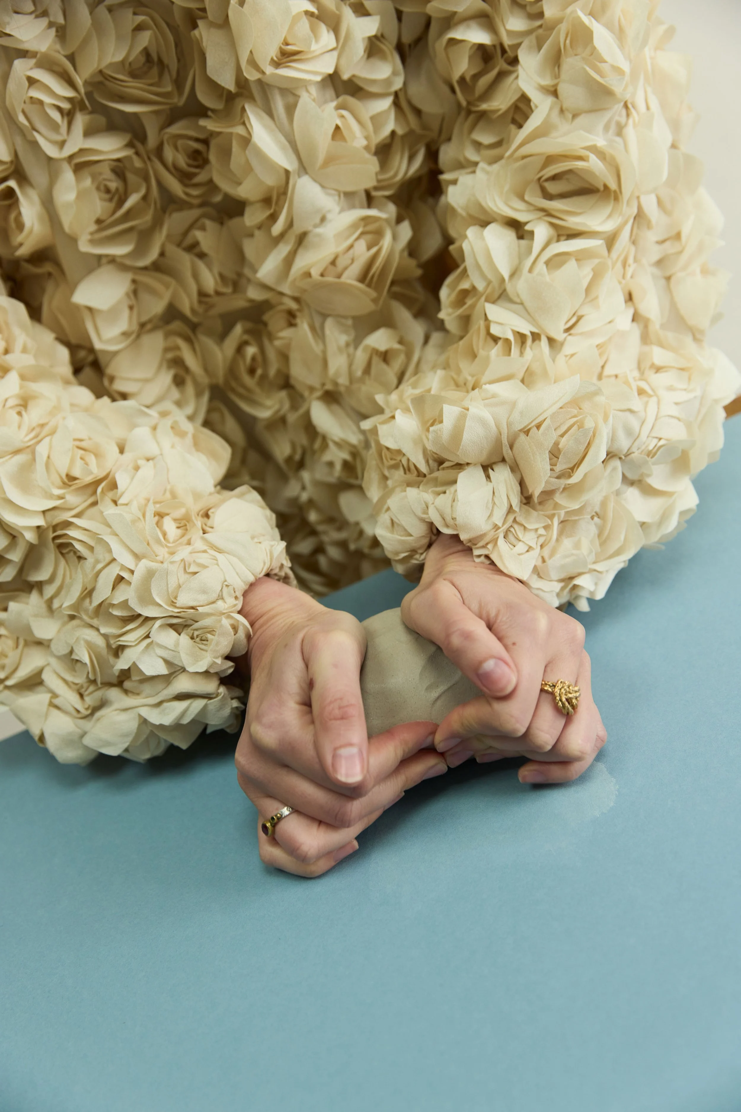 Une personne porte un pull beige à textures en forme de fleurs en enroulant de l'argile dans ses mains.