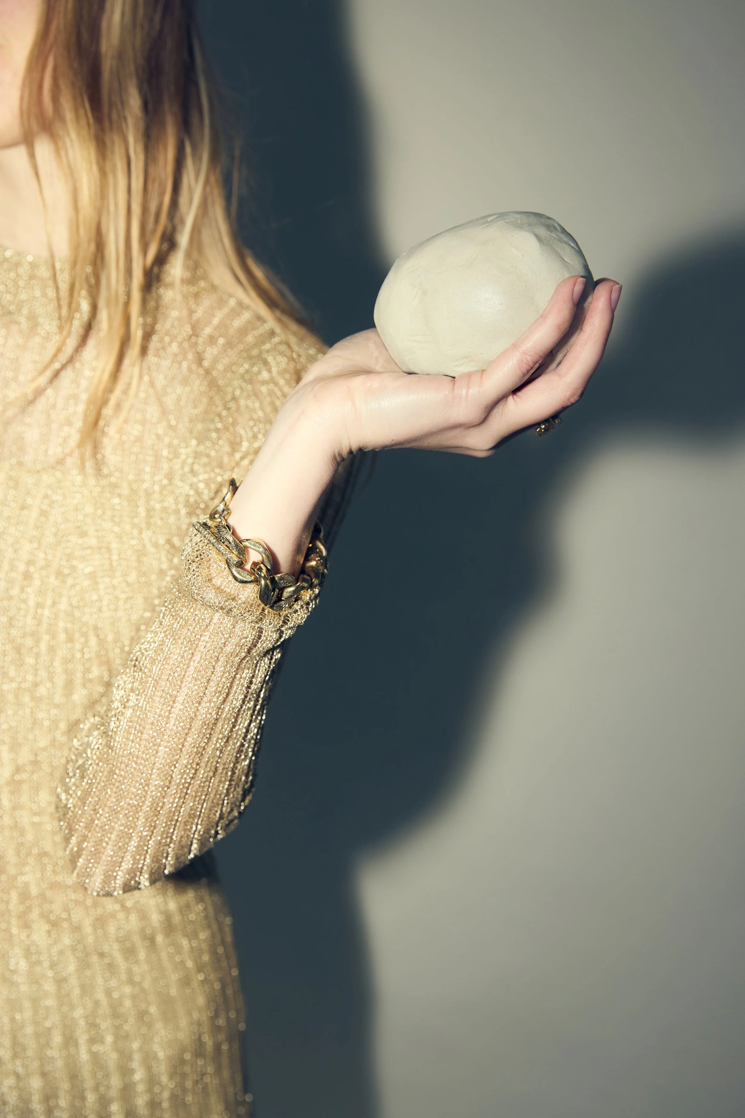 Une femme portant une robe dorée, tenant une pierre blanche dans sa main, avec un bracelet doré.