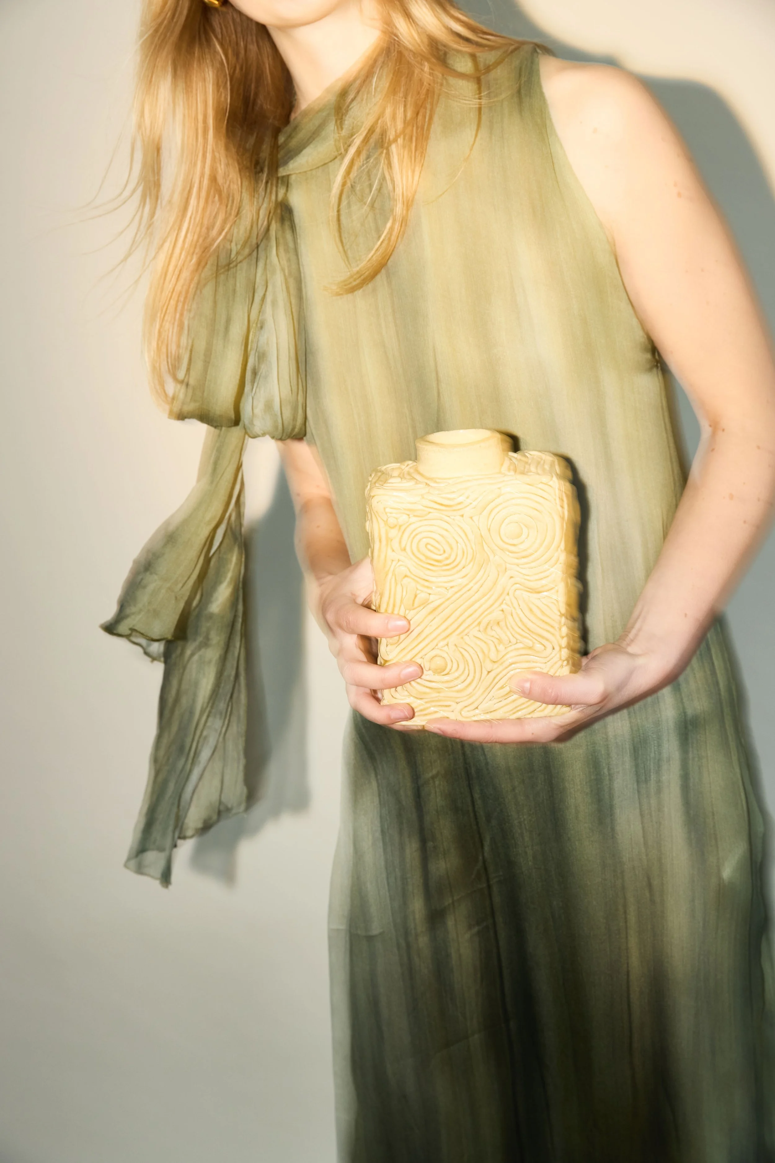 Femme tenant un vase en céramique de couleur beige avec un motif de lignes en relief.