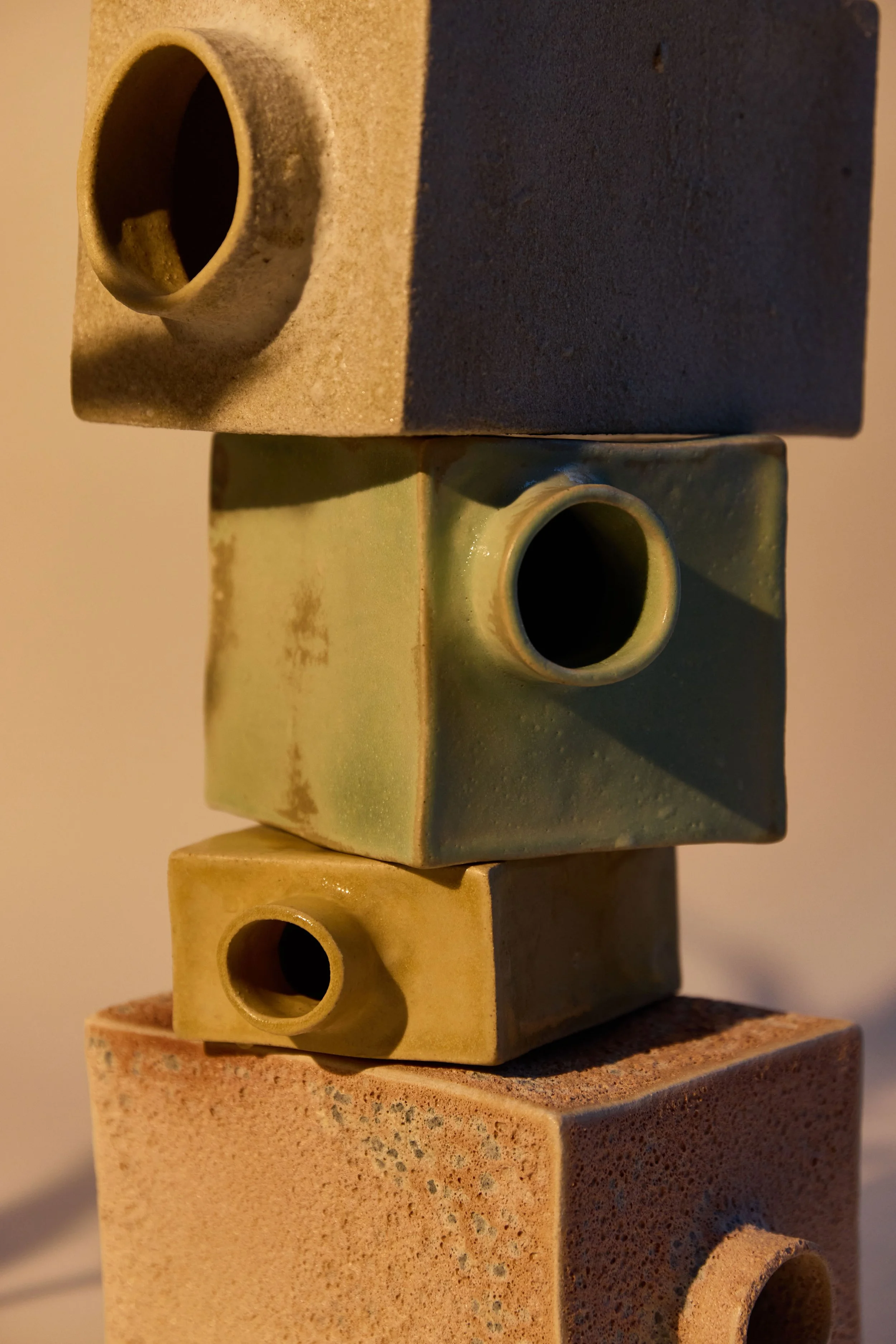 Une sculpture composée de quatre cubes en terre cuite empilés, avec des tubes de céramique insérés dans certains côtés, formant une structure abstraite.