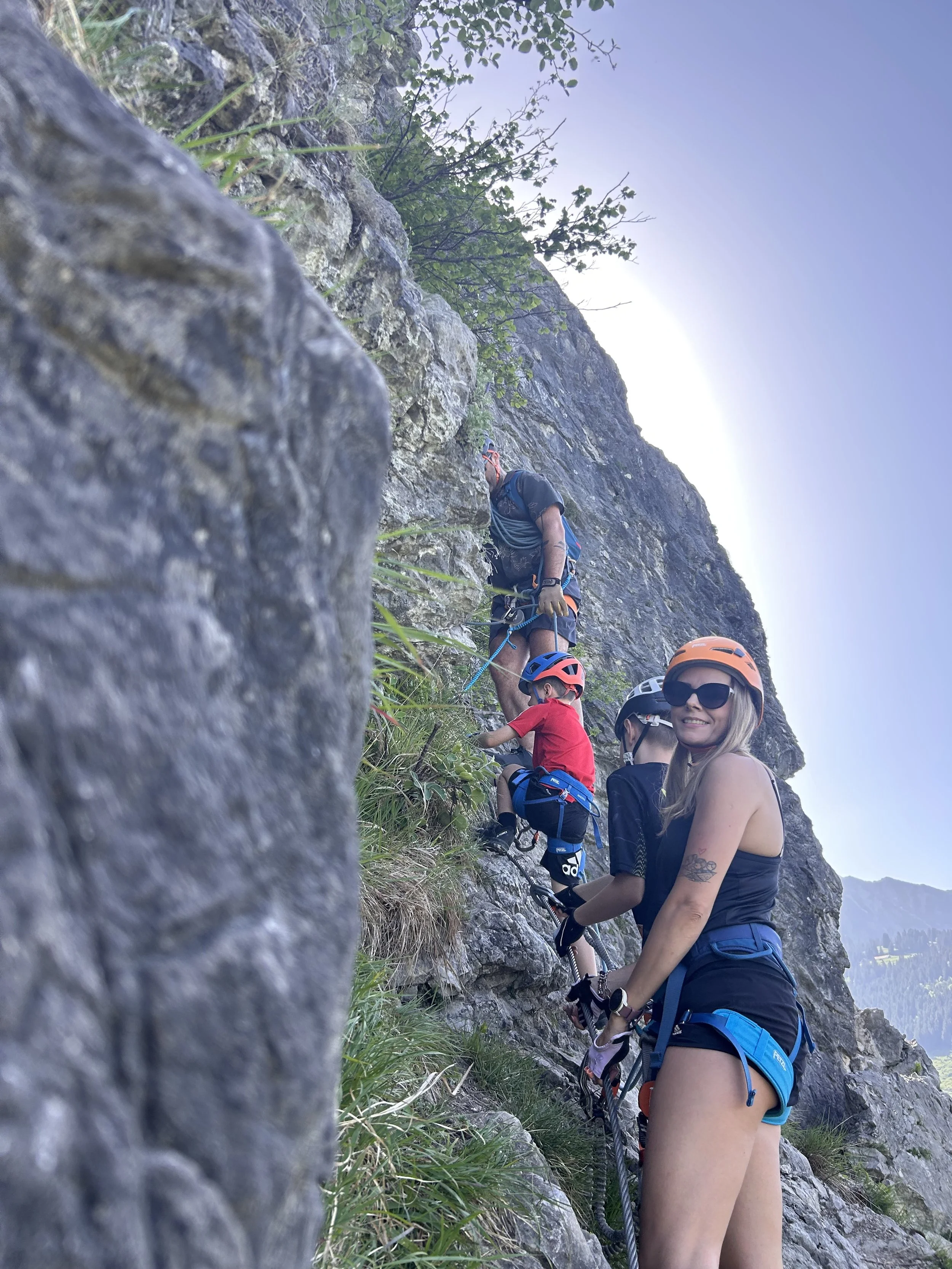 A climbing instructor explaining safety procedures to two climbers on a rock face outdoors, all wearing helmets and harnesses.
