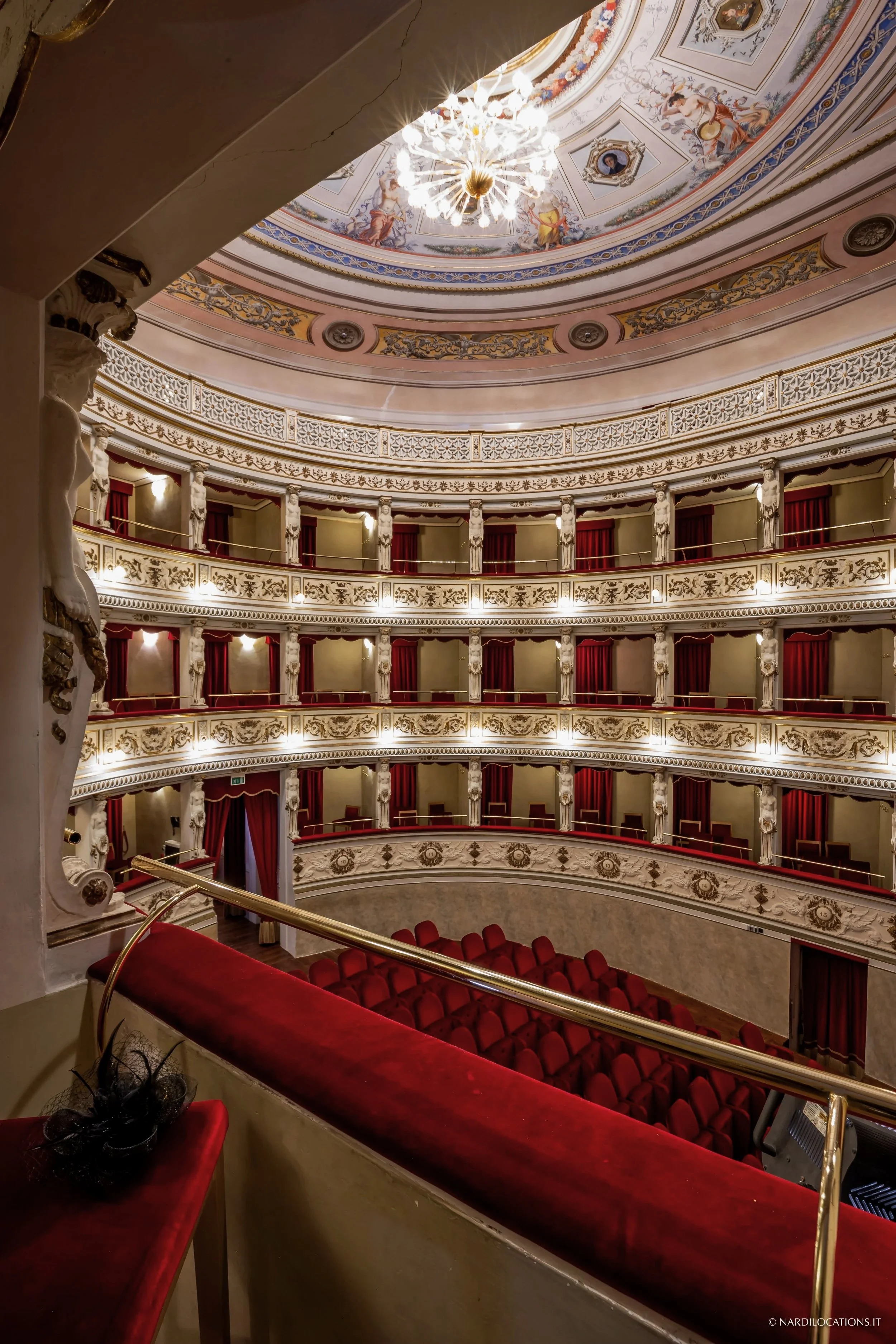 Interno del Teatro Domenico Alaleona con palchi e sedili rossi, decorazioni dorate e un soffitto dipinto con affreschi e un lampadario centrale.