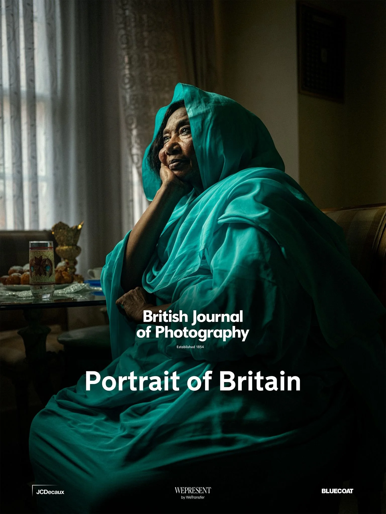 Book cover titled 'Portrait of Britain' from the British Journal of Photography featuring a portrait of an elderly woman wearing a teal headscarf and robe, sitting in a softly lit room with a table of snacks and a cup in the background.
