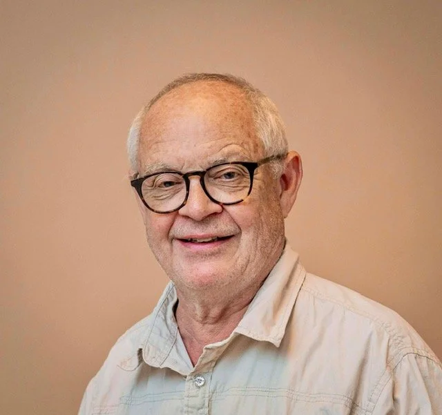 Sort-hvid portrætfotokopi af en ældre mand med kort gråt hår og briller, iført en plaid skjorte og en sweater.