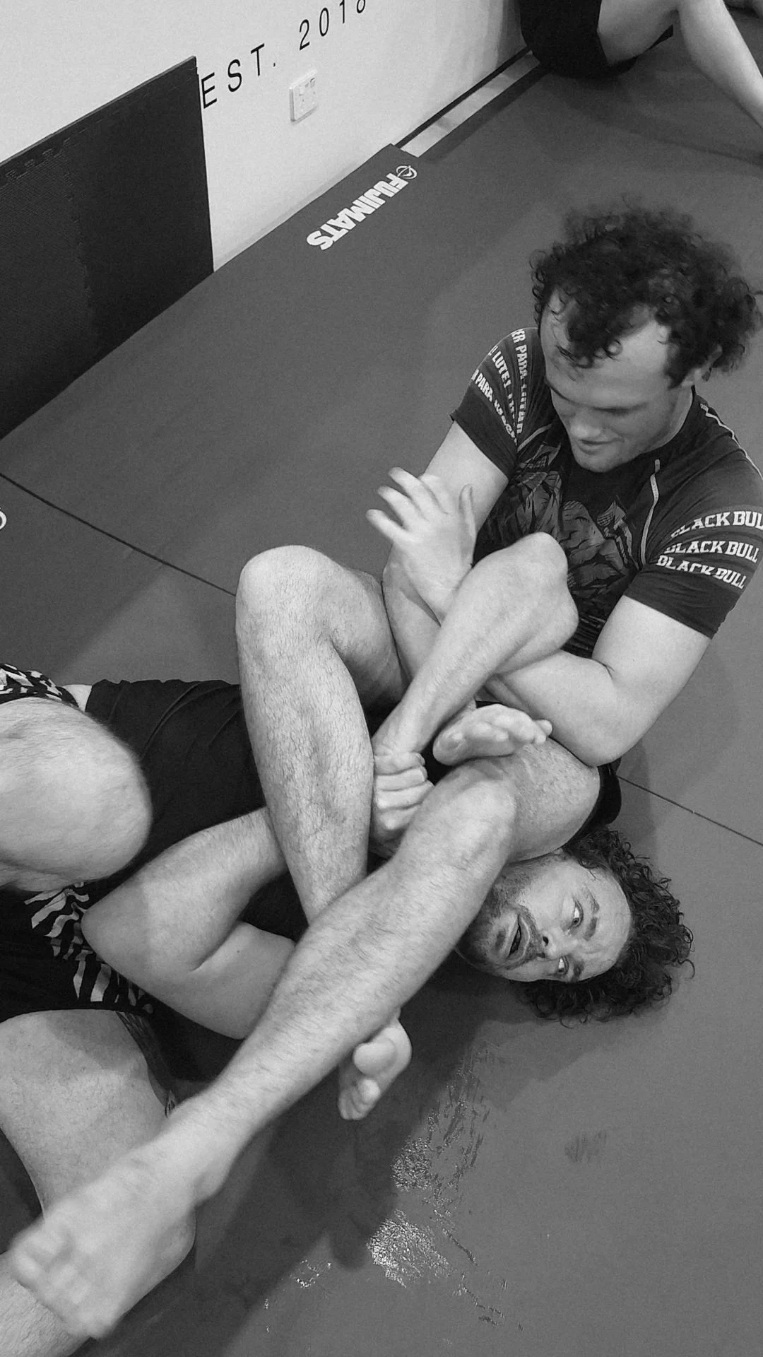 Two men practicing Brazilian Jiu-Jitsu on a mat, one attempting to control the other during a grappling match.